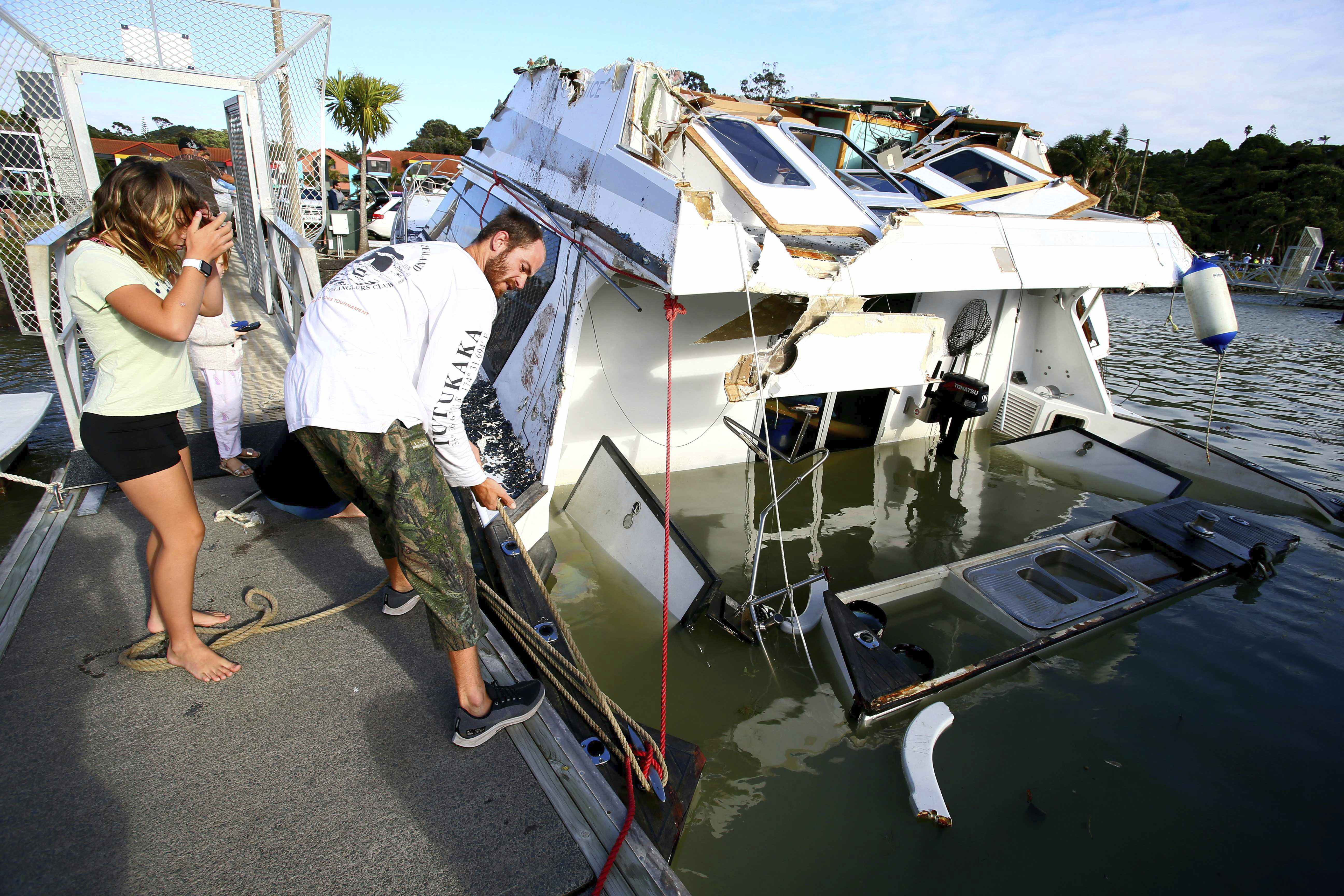 A couple look at a damaged boat in a marina at Tutukaka, New Zealand