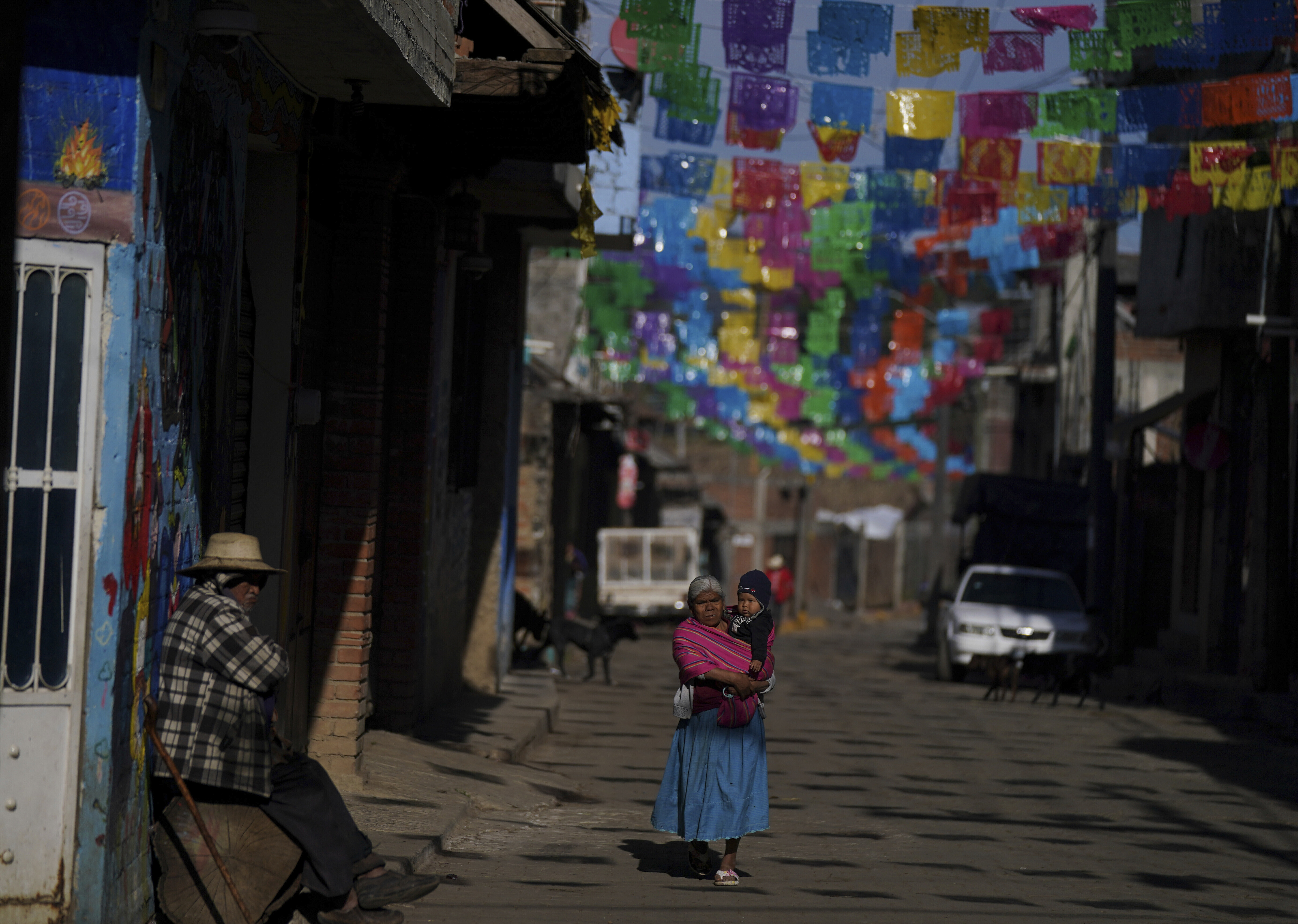 Residents walk along a street decorated with elaborately cut colored pieces of tissue paper called “papel picado, in the Puerpecha Indigenous community of Comachuen, Mexico