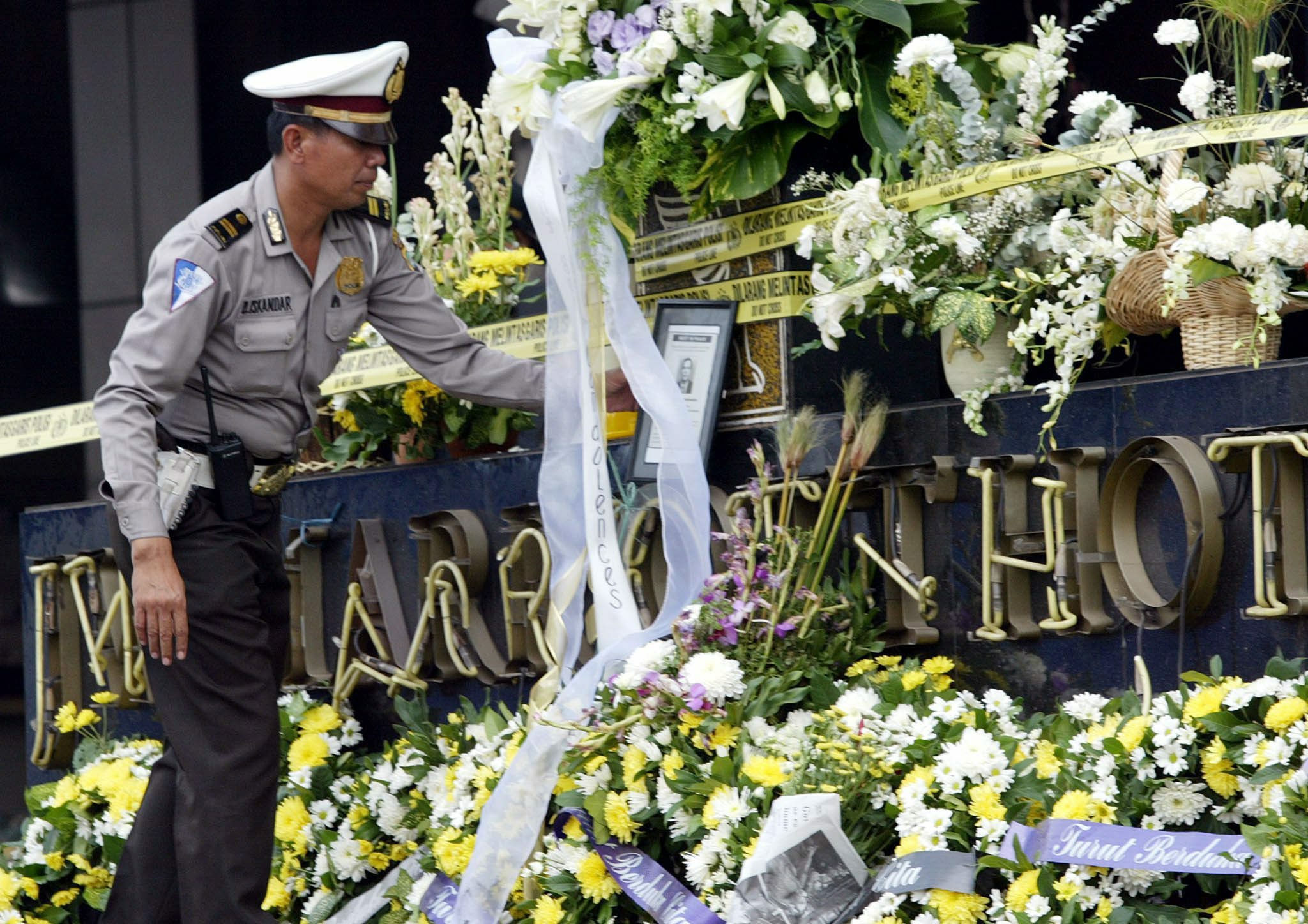 An Indonesian police officer looks at the bouquets of white flowers left at the mangled signboard of Jakarta's JW Marriott Hotel as prayers were hekd for those killed in the August 2003 bombing