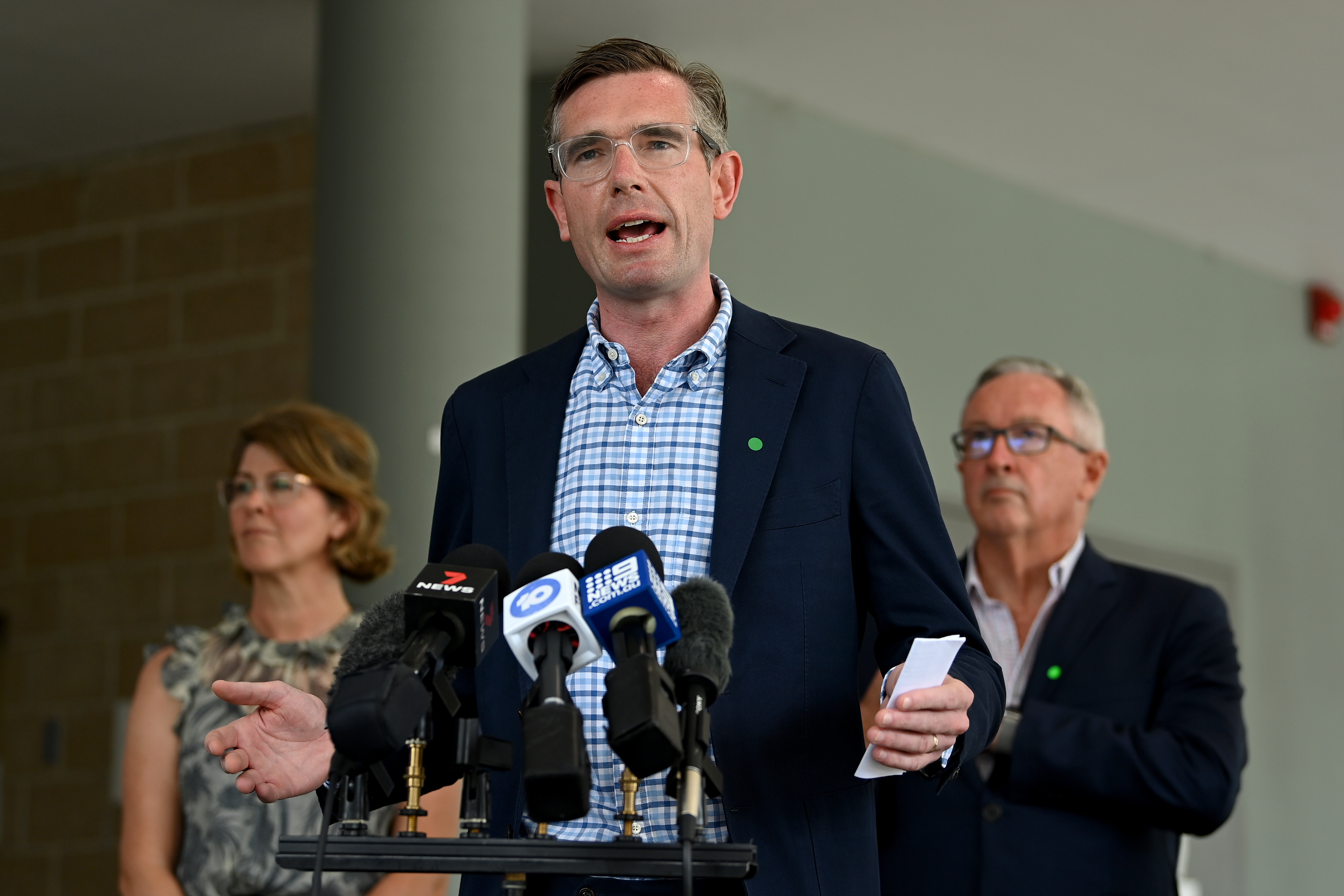 NSW Premier Dominic Perrottet in a blue suit and pale blue shirt tands at a lectern and speaks to the media 