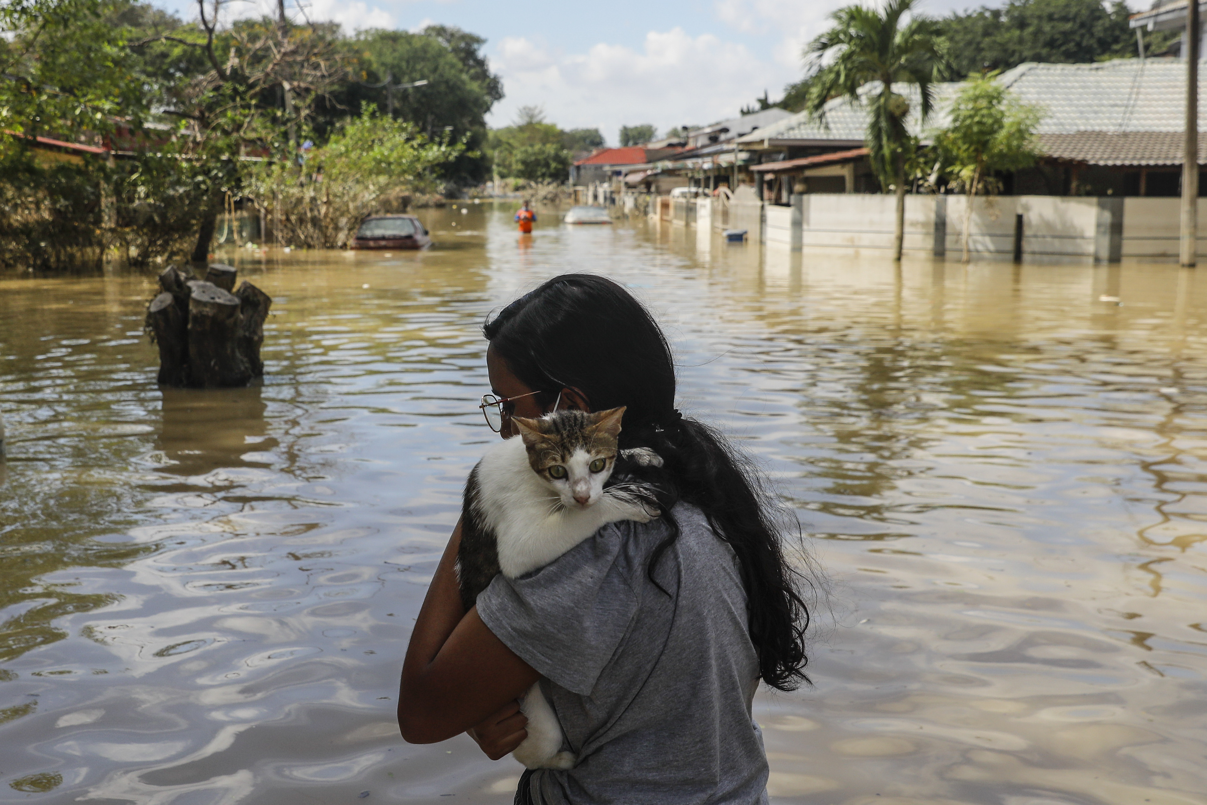 A woman carrying her tortoiseshell cat on her shoulder as she wades through milky brown floodwaters in the Malaysian city of Shah Alam