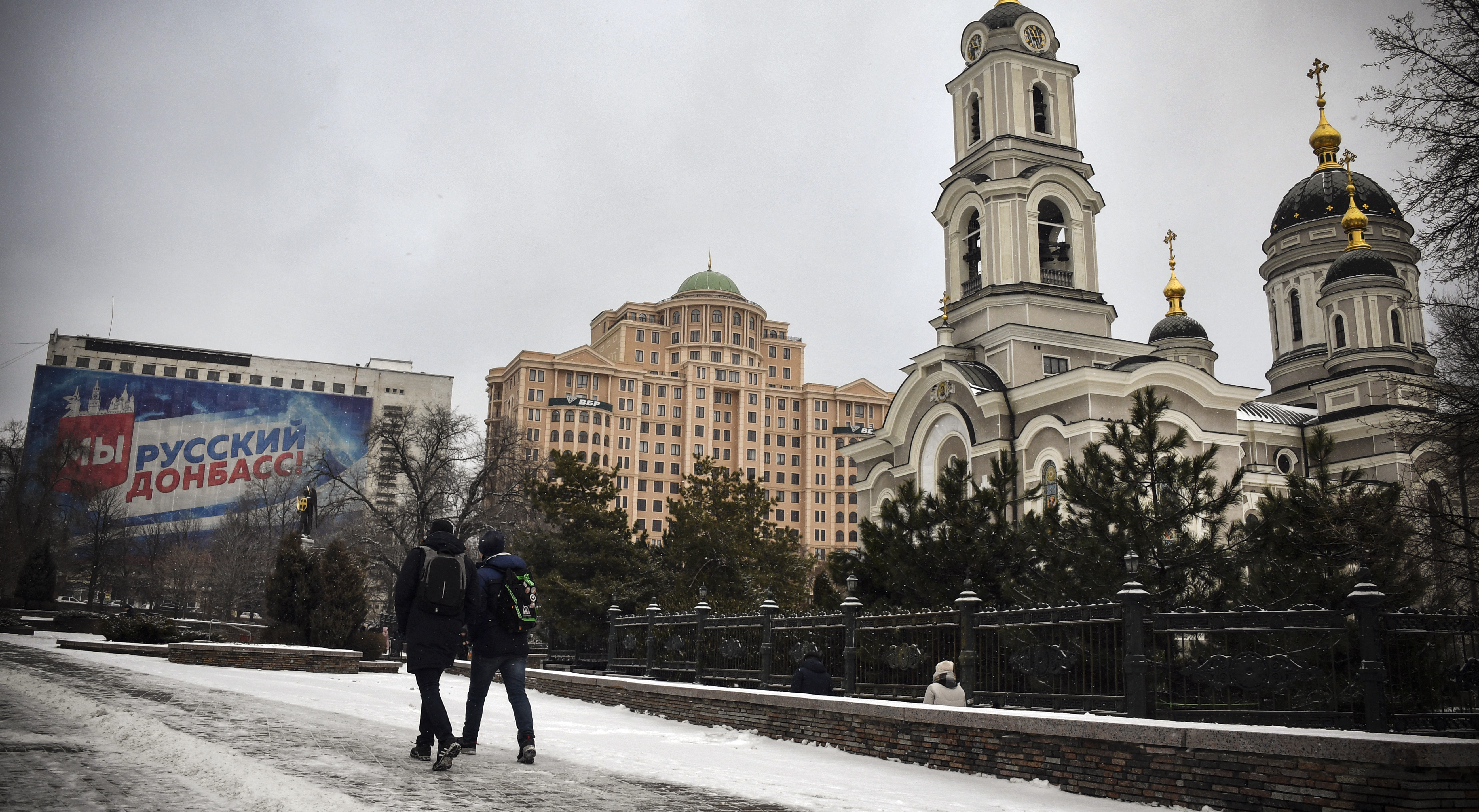 Pedestrians walk in central Donetsk, eastern Ukraine, the capital of a self-proclaimed Donetsk People's Republic (DPR), on January 19, 2022. - A poster on the left reads: "We Are the Russian Donbass!". (Photo by Alexander NEMENOV / AFP)