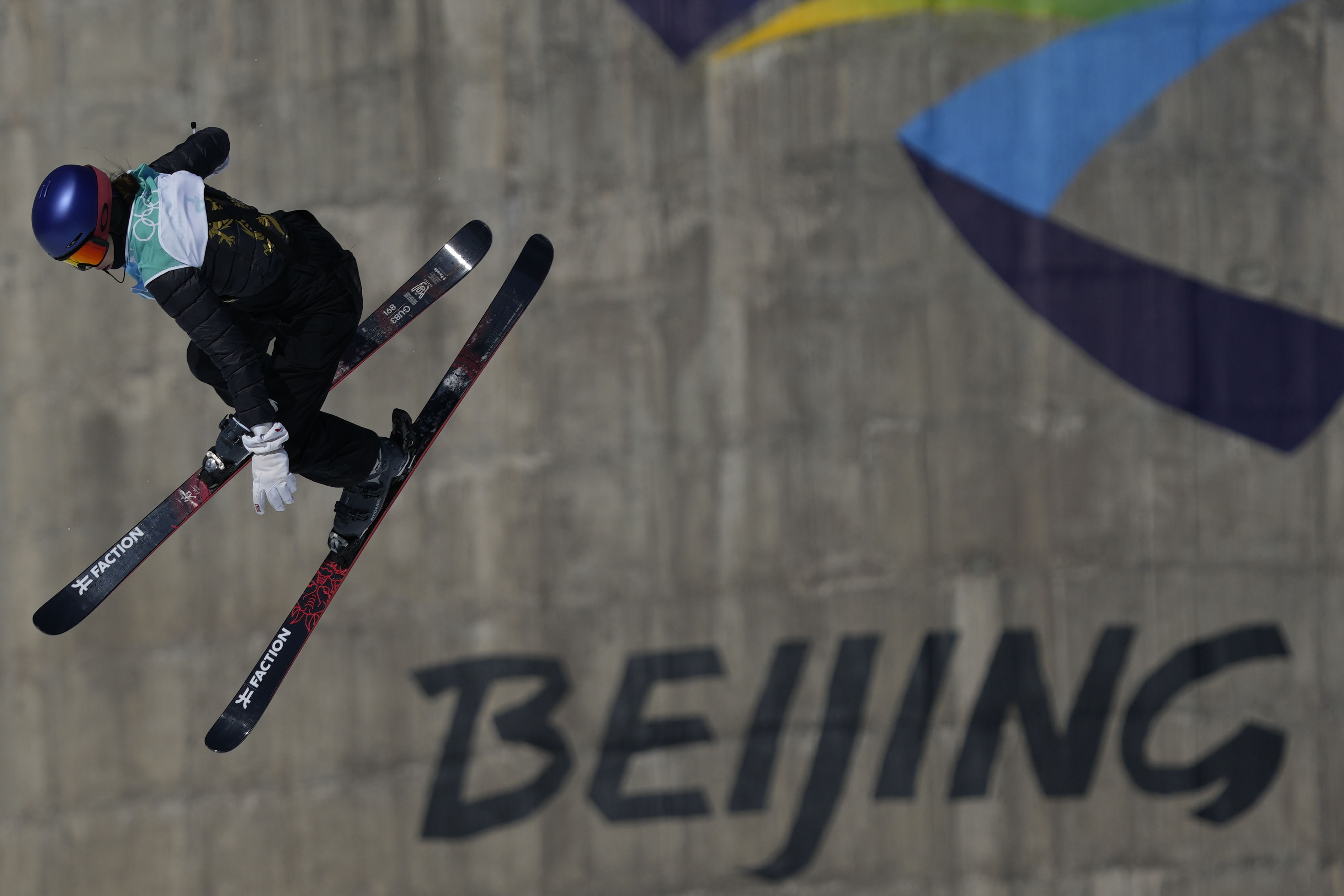Eileen Gu pictured mid-air in front of a grey concrete wall emblazoned with the Beijing Winter Olympics logo