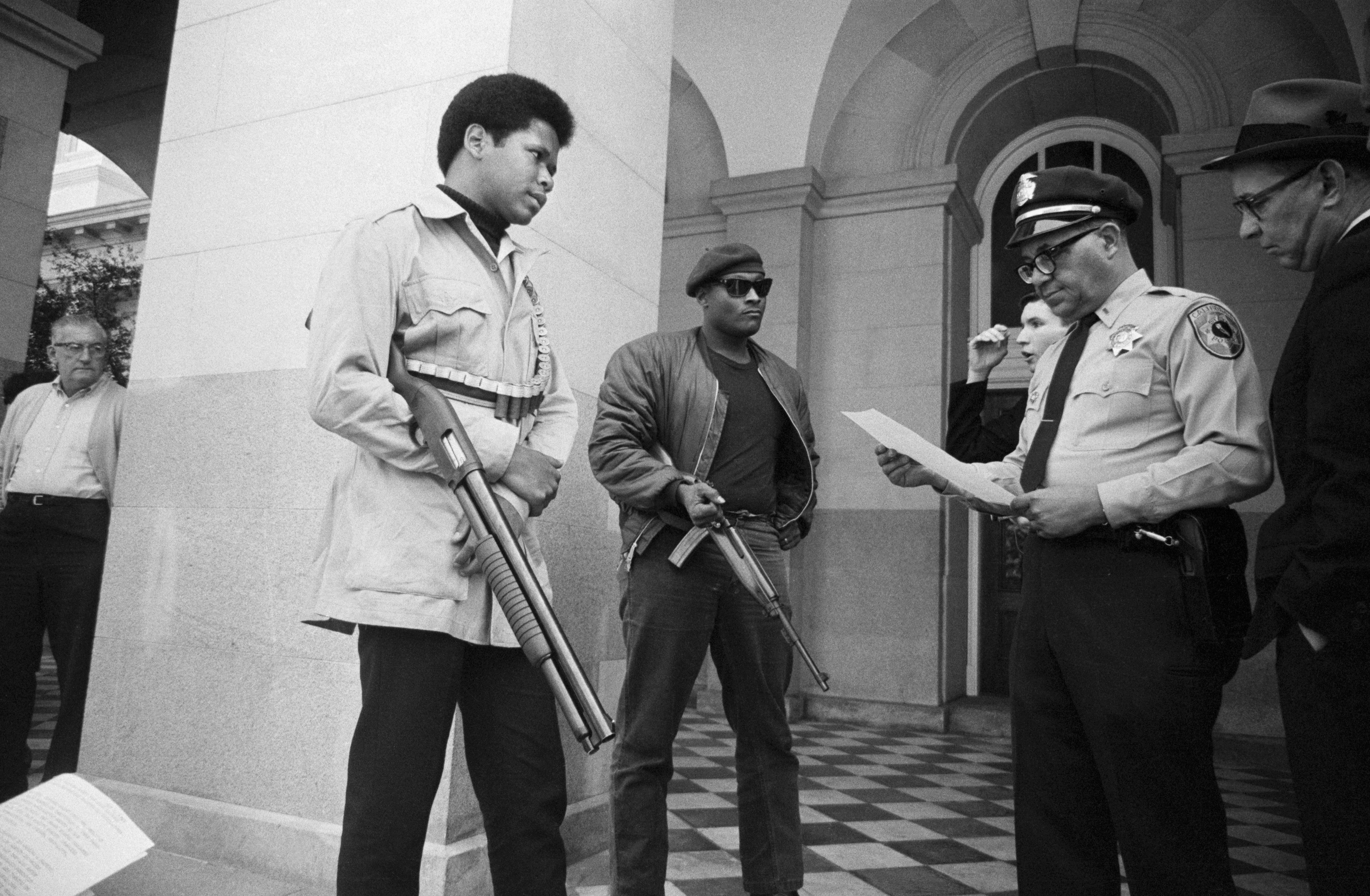 Two members of the Black Panther Party and a policeman on the steps of the State Capitol in Sacramento in 1967