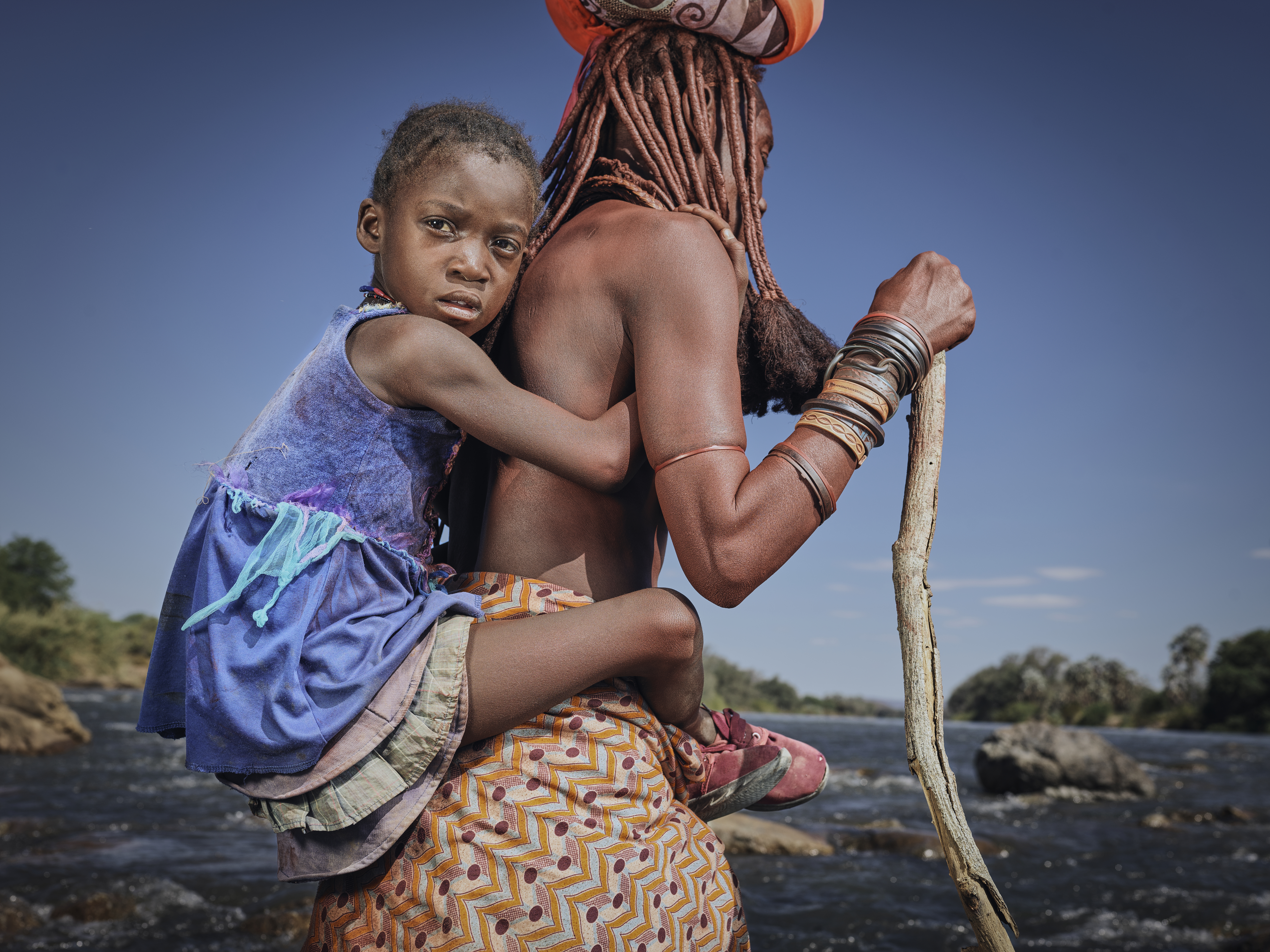 A photo of a woman holding a cane, carrying a child on her back.