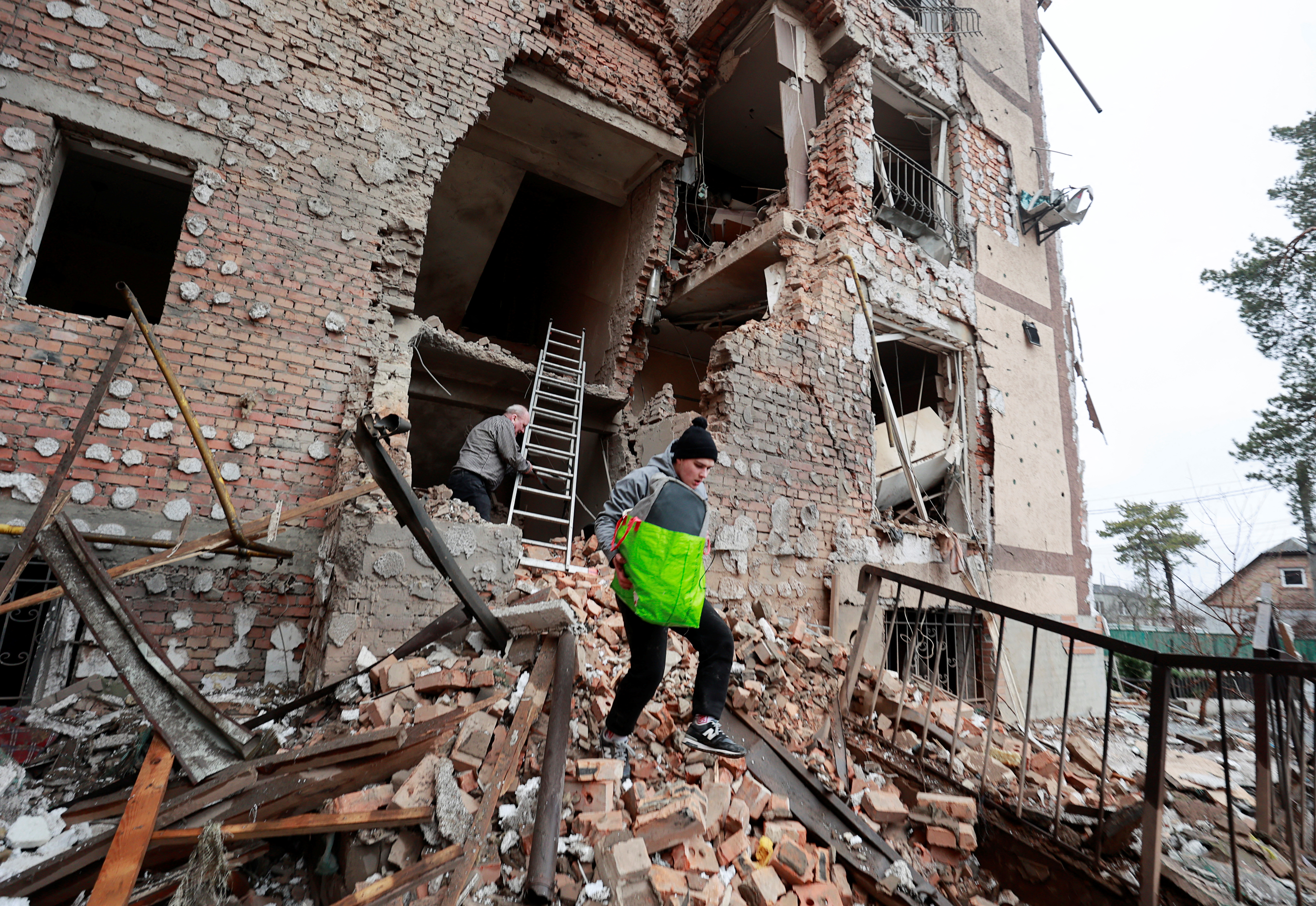 People are seen carrying belongings out of a residential building destroyed by shelling