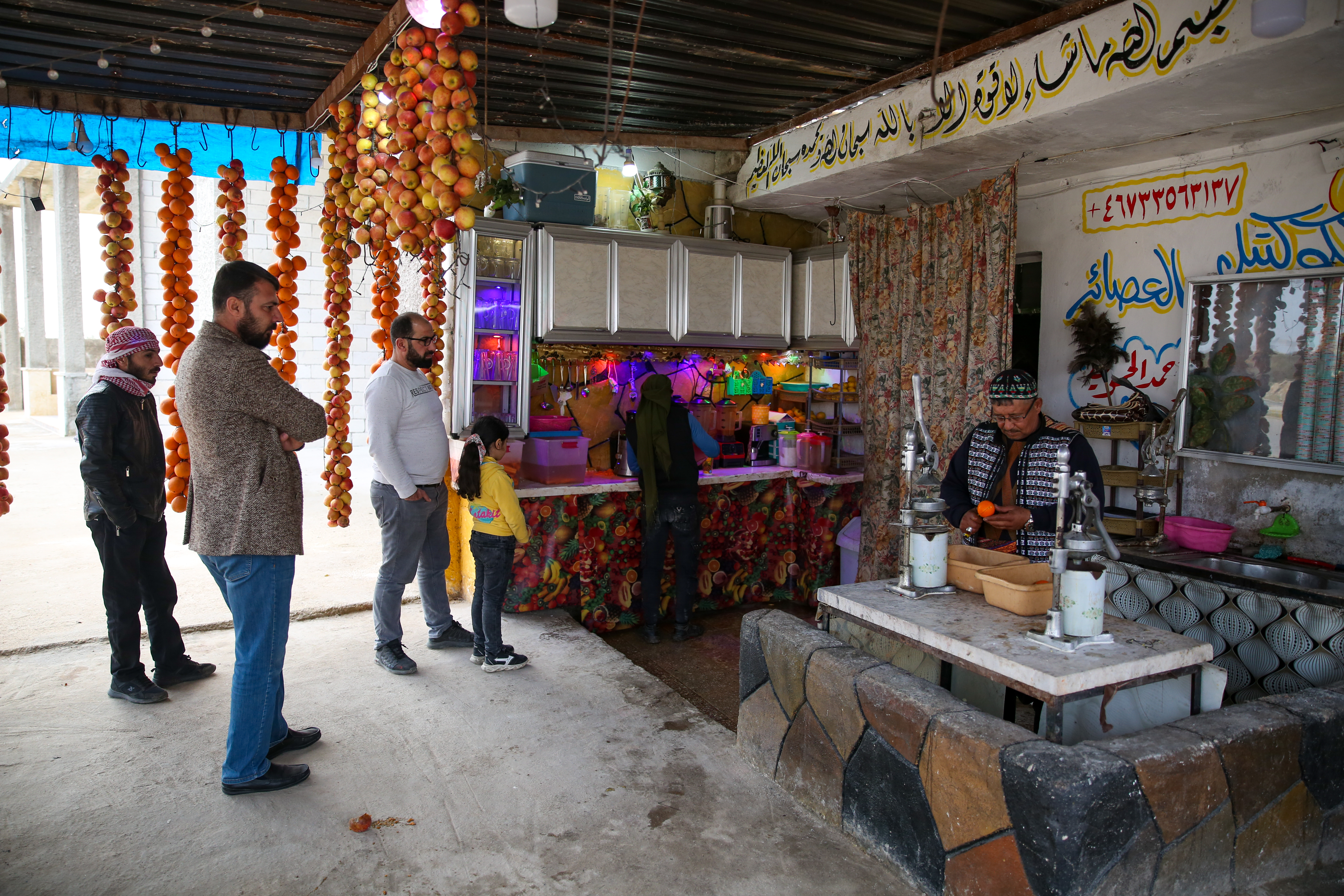 Daaboul is making orange juice behind a counter while four customers wait beneath garlands of drying fruit for their drinks