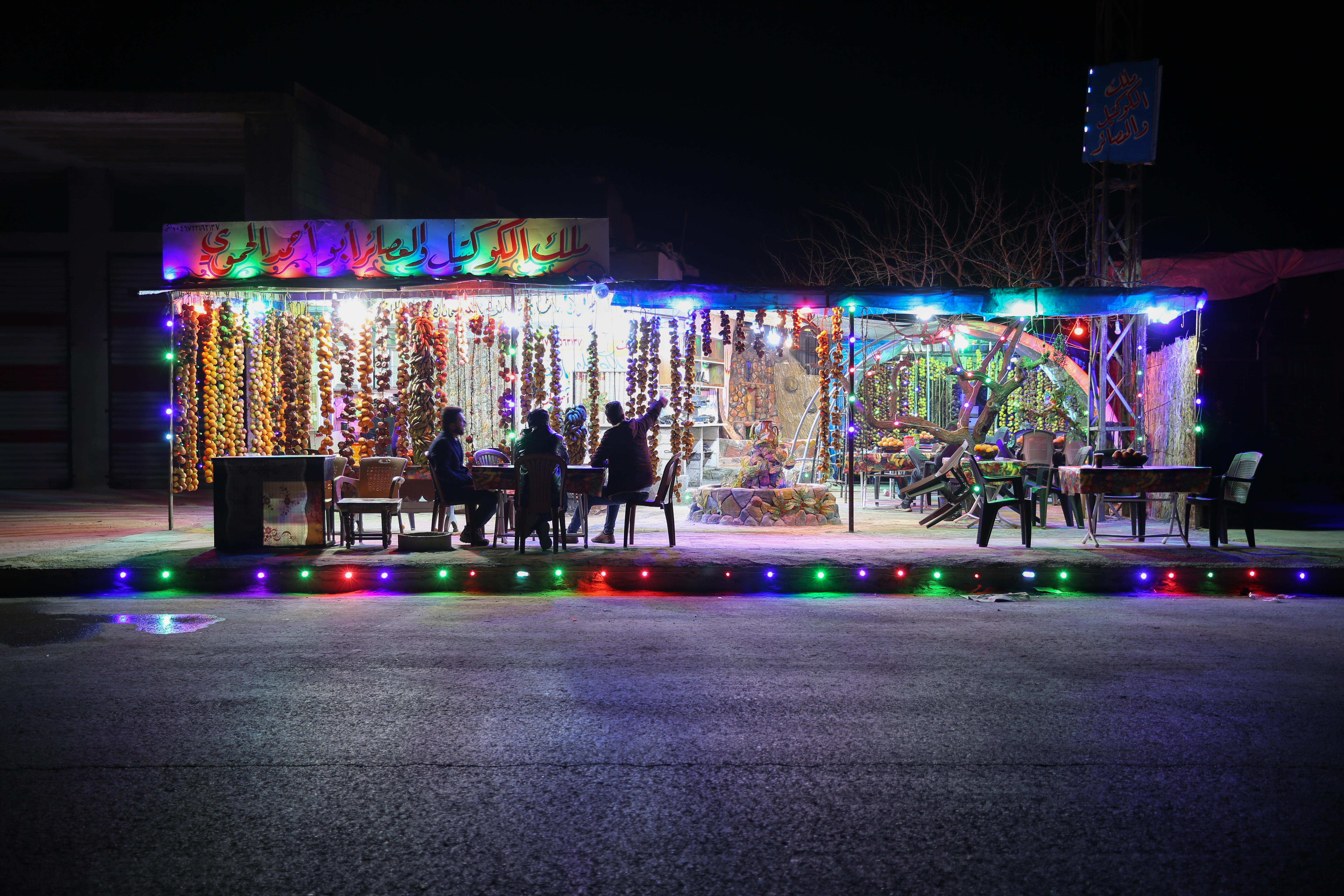 A night view of the front of Daaboul's juice shop, lit up in an otherwise dark street. A table of customers is out front