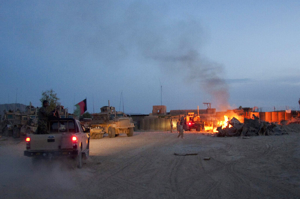 an Afghan National Army pickup truck passes parked U.S. armored military vehicles, as smoke rises from a fire in a trash burn pit at Forward Operating Base Caferetta Nawzad, Helmand province south of Kabul, Afghanistan.