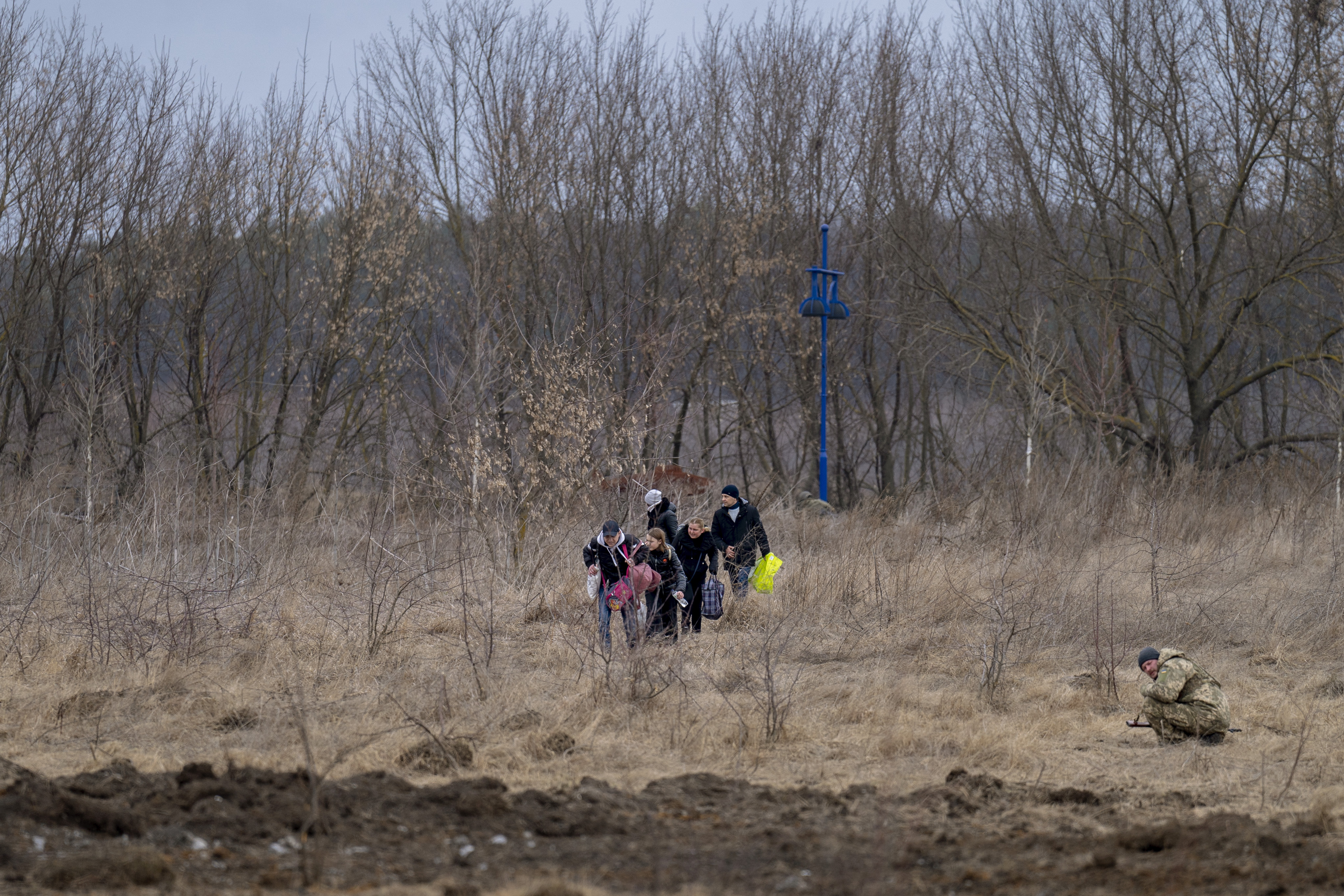 A Ukrainian soldier covers himself as the artillery echoes nearby, while people flee Irpin on the outskirts of Kyiv