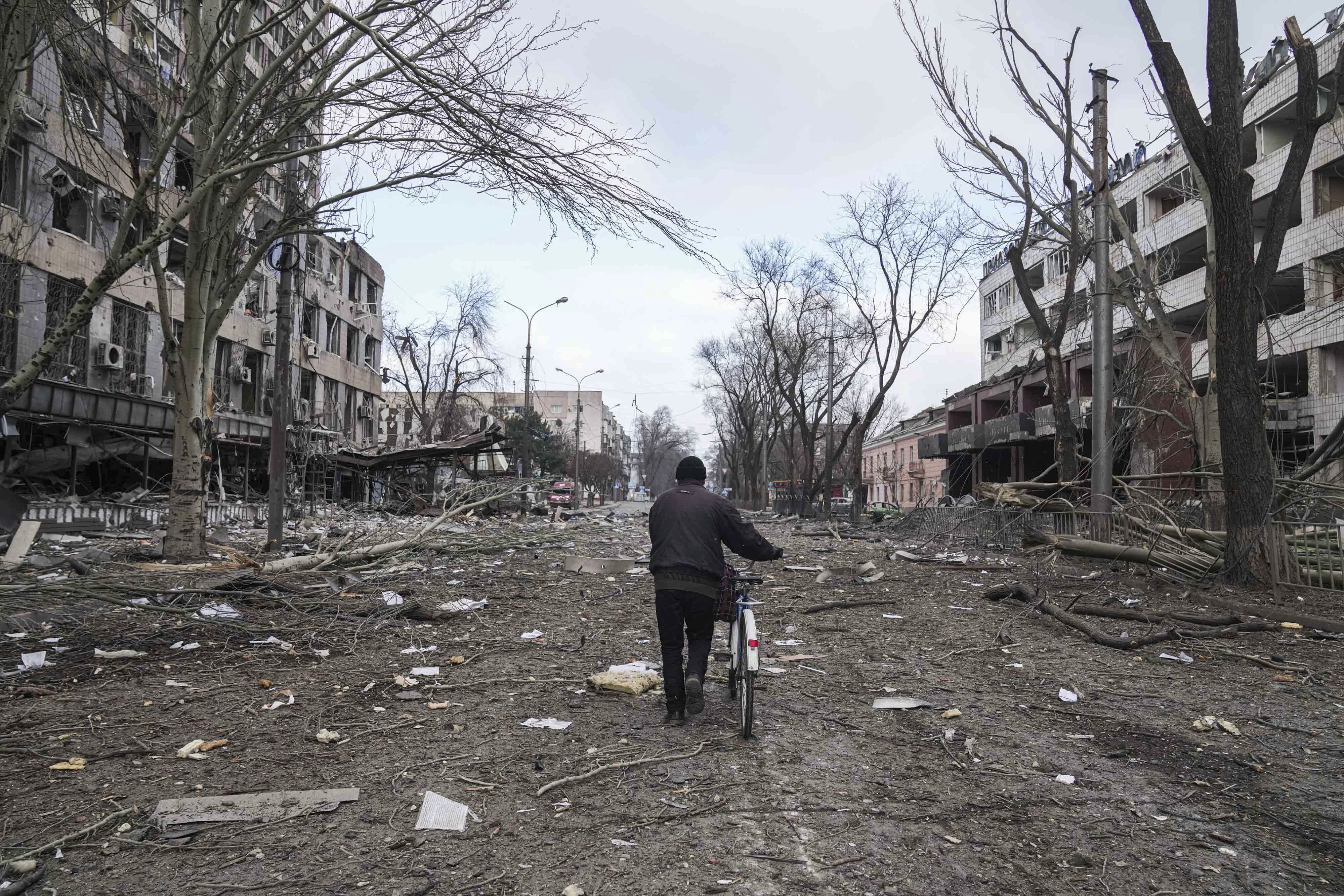 A man walks with a bicycle in a street damaged by shelling in Mariupol, Ukraine