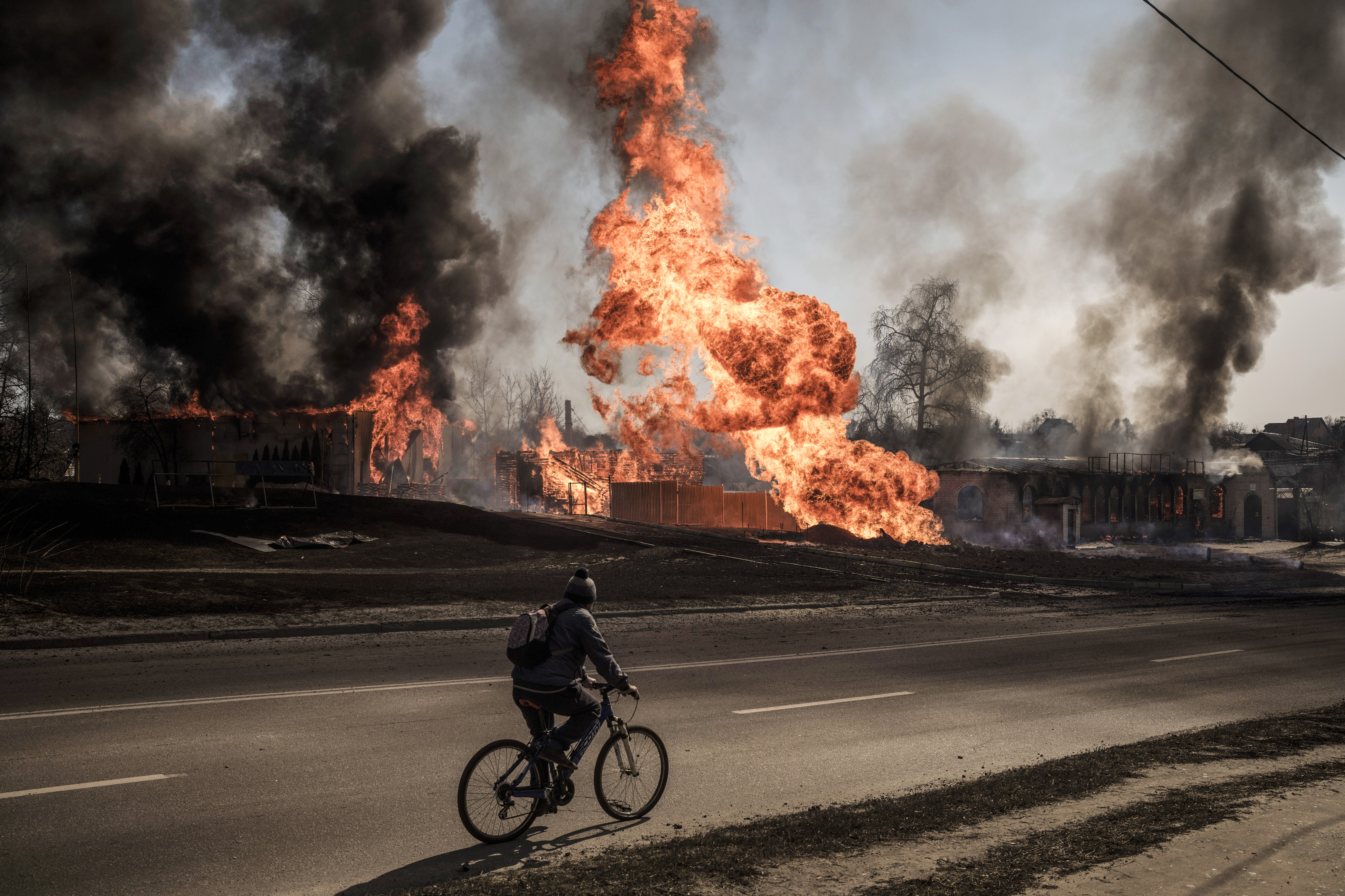 A man rides his bike past flames and smoke rising from a fire following a Russian attack in Kharkiv