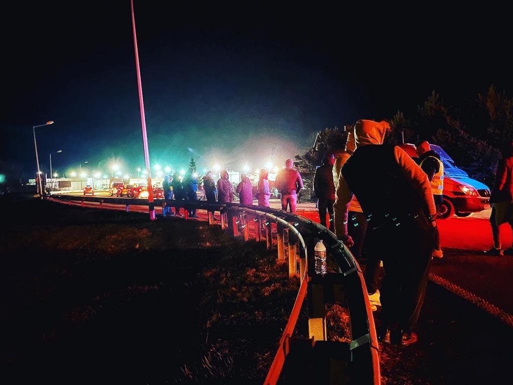 A photo of a line of people in the street at night.