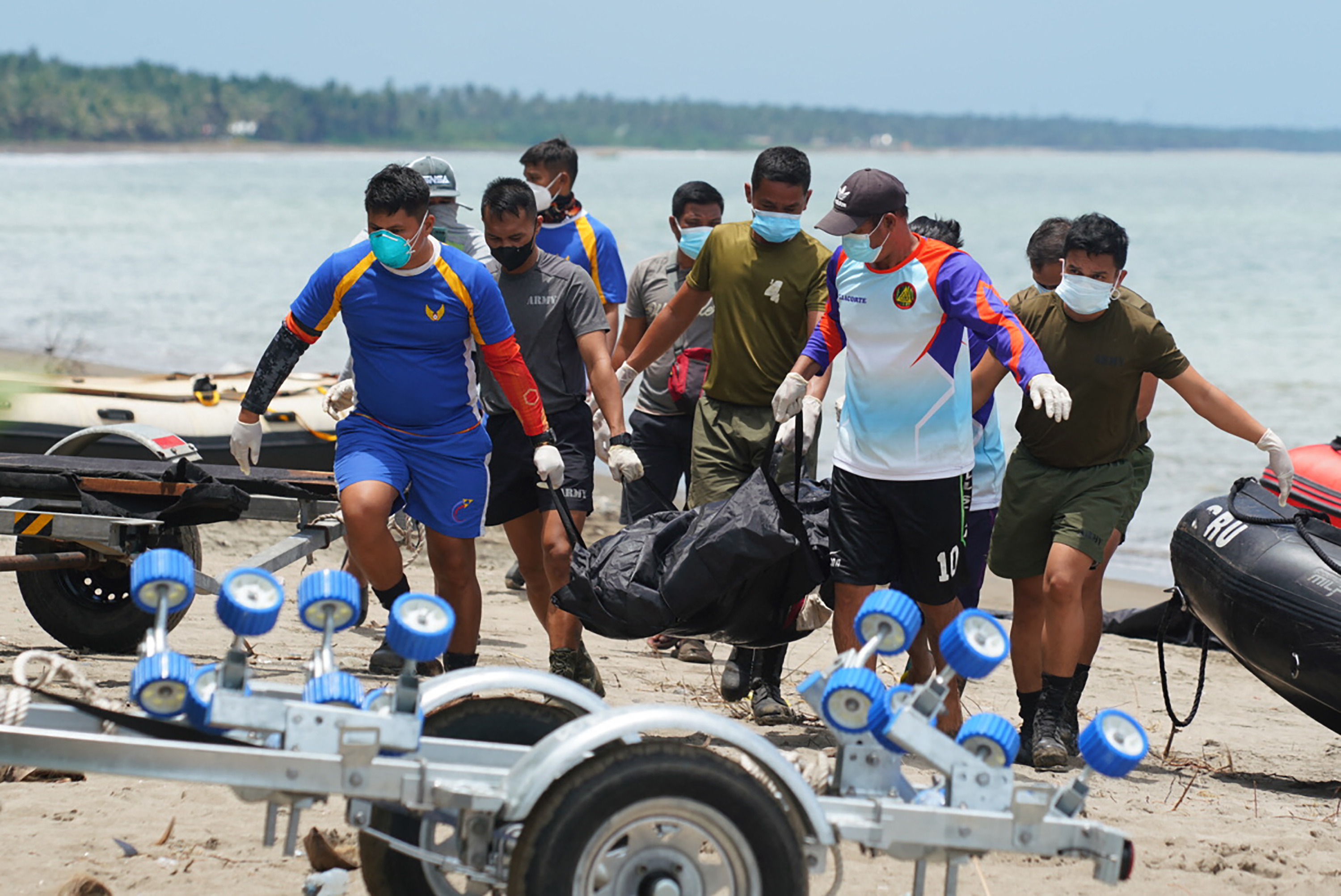 A group of rescuers carry a body in a black tarpaulin along a beach after Tropical Storm Megi