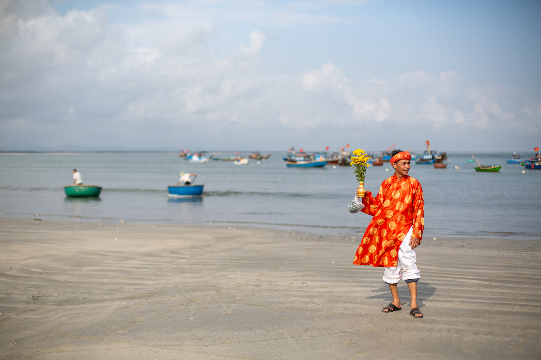 A photo of a whale worshipper dressed in a red-and-crimson áo dài holding flowers on the beach.