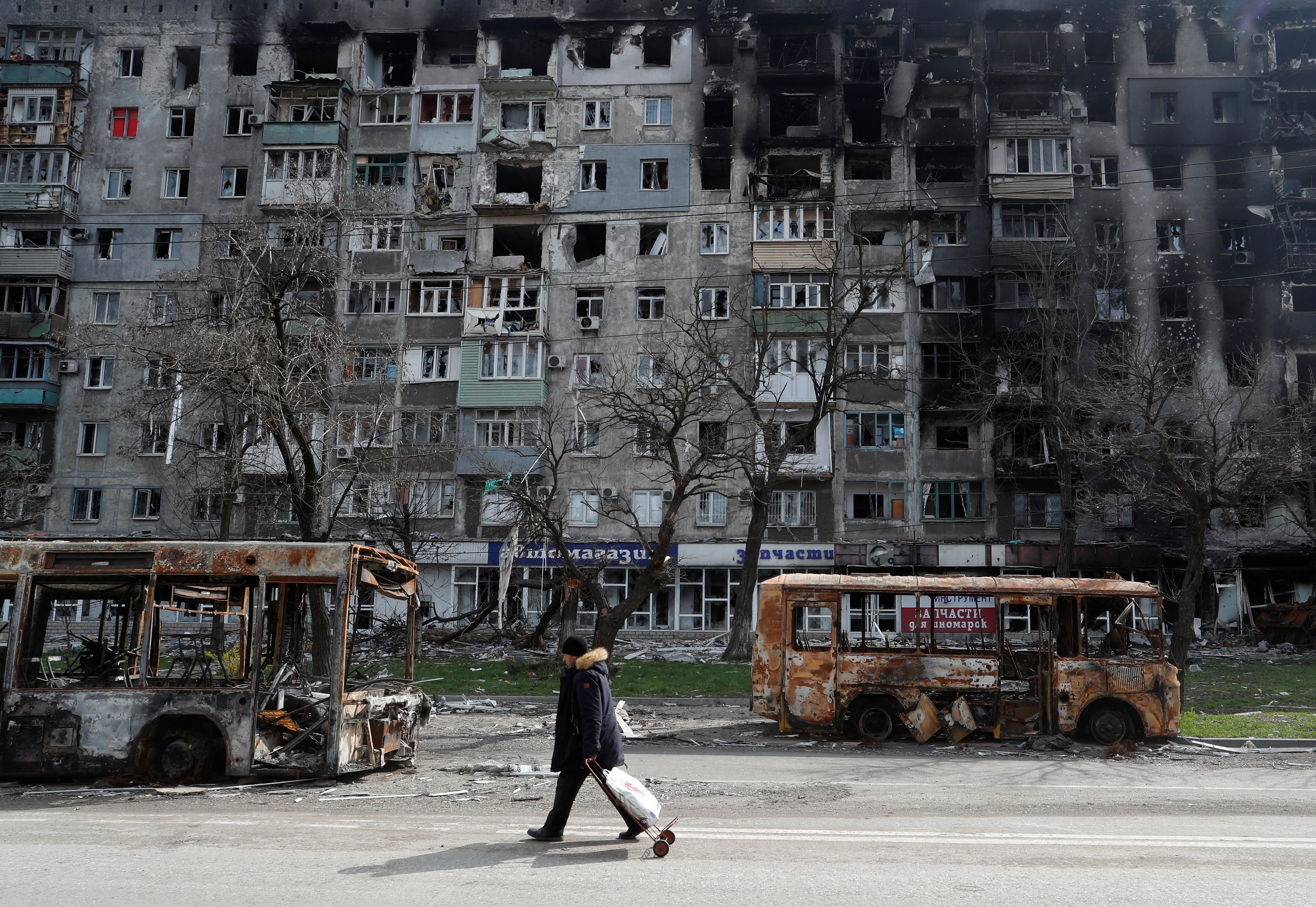 A local resident walks along a street past burnt out buses during Ukraine-Russia conflict in the southern port city of Mariupol.