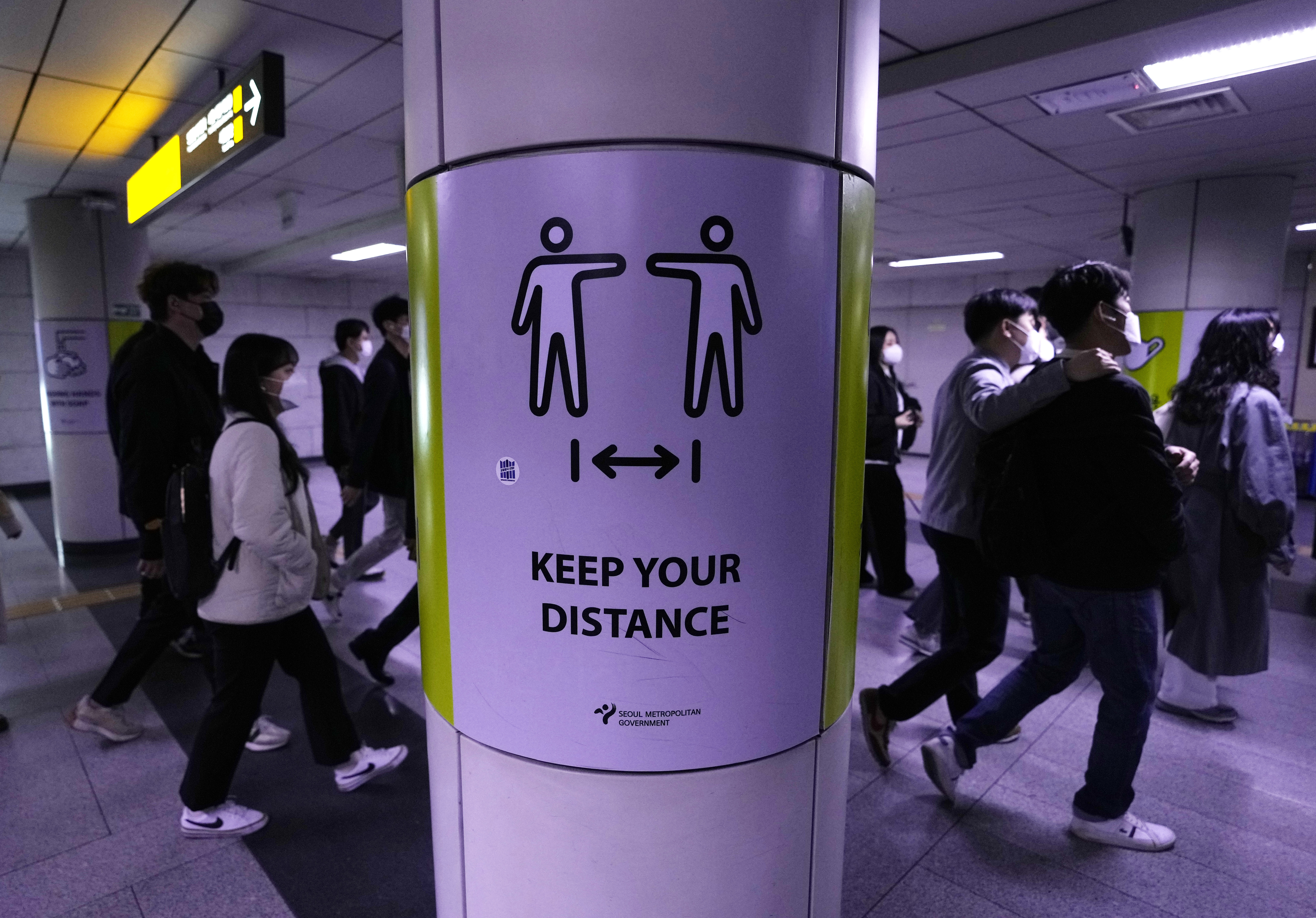 People wearing face masks pass by a poster reminding precautions against the coronavirus at a subway station in Seoul,