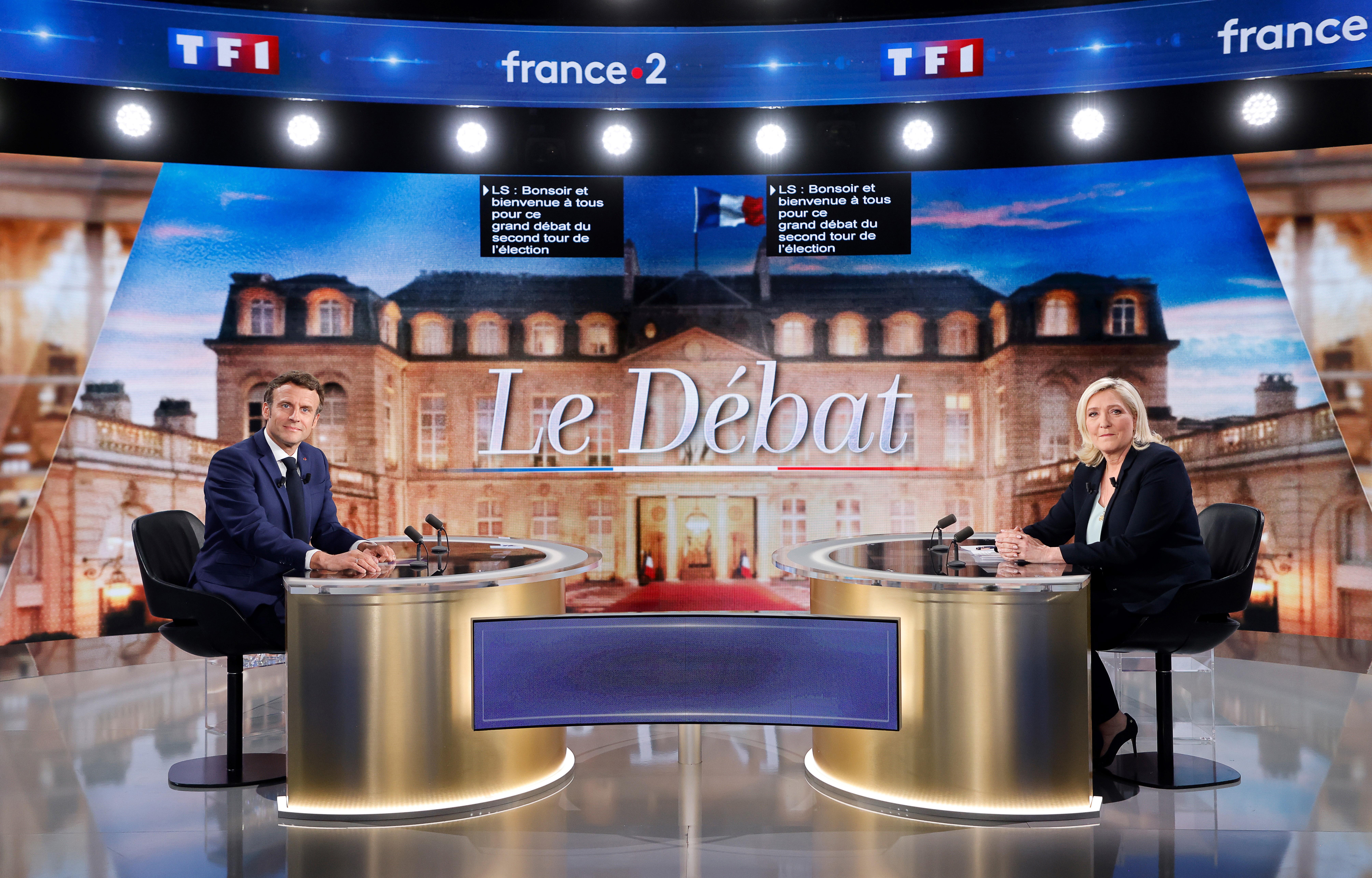 Emmanuel Macron and Marine Le Pen face each other from golden coloured tables against a picture of the Elysee Palace and the words 'Le Debat' ahead of the candidates single debate before Sunday's election.