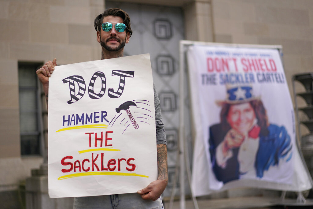 Nicholas Rivers of Maine, holds a sign that reads DOJ Hammer the Sacklers” during a protest with advocates for opioid victims outside the Department of Justice