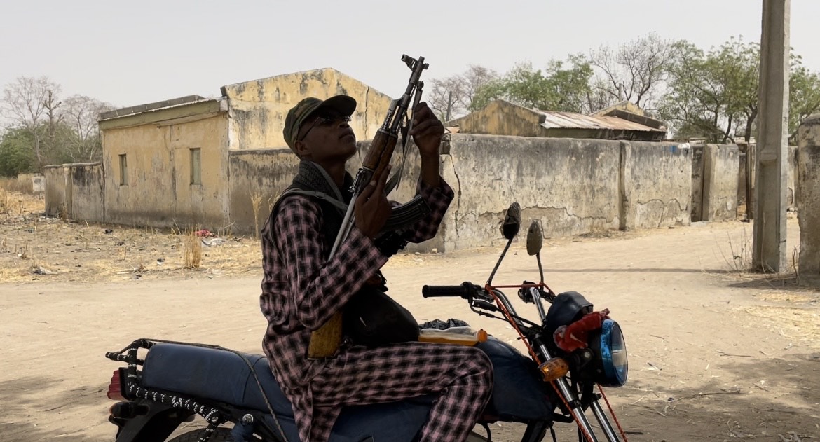 A bandit plays with his rifle under a tree