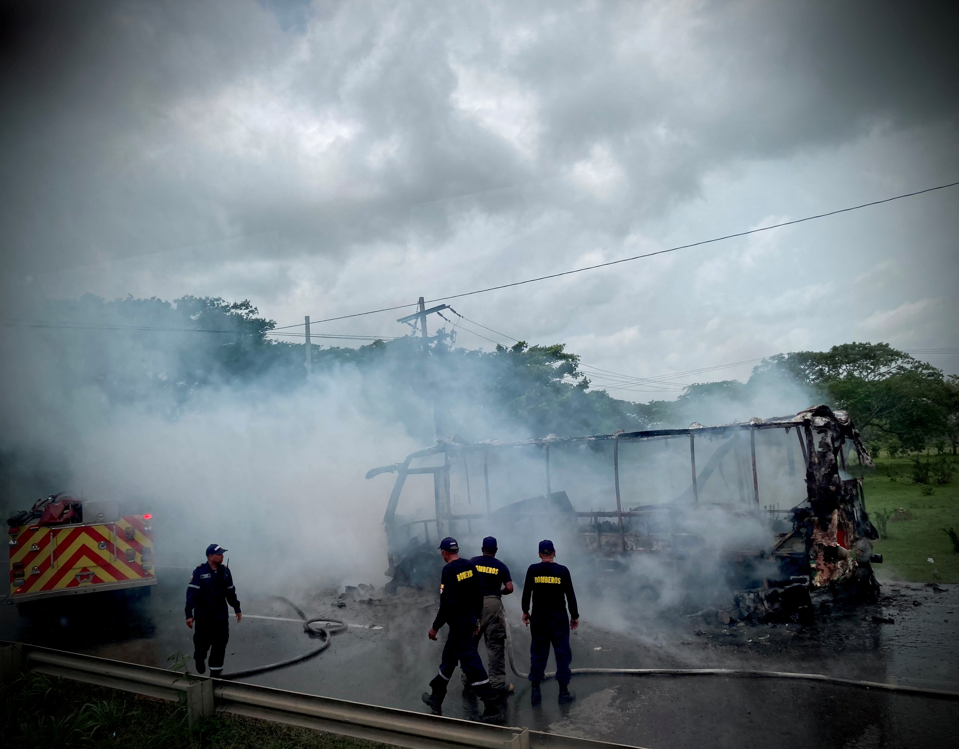 Firefighters stand by a burnt vehicle