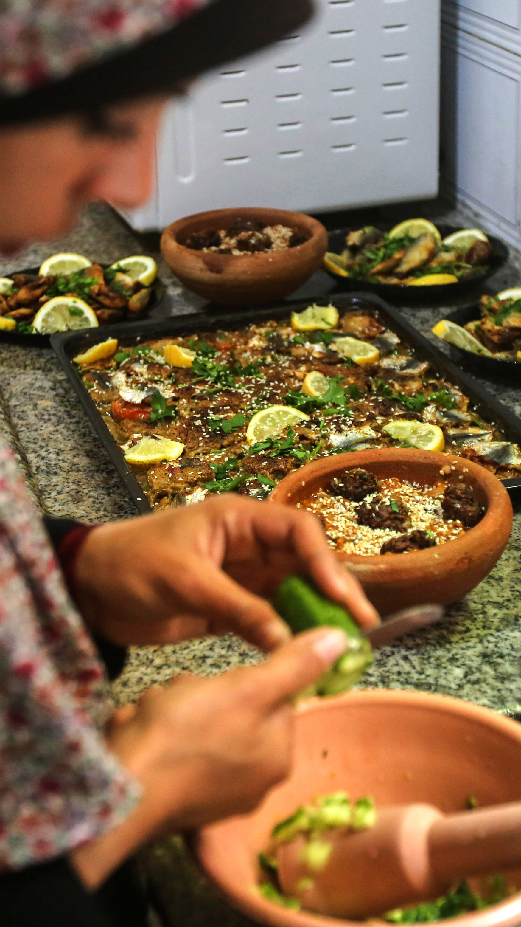 Madelyn is in the foreground chopping vegetables into a mortar while in the background dishes for the meal are laid out on the counter