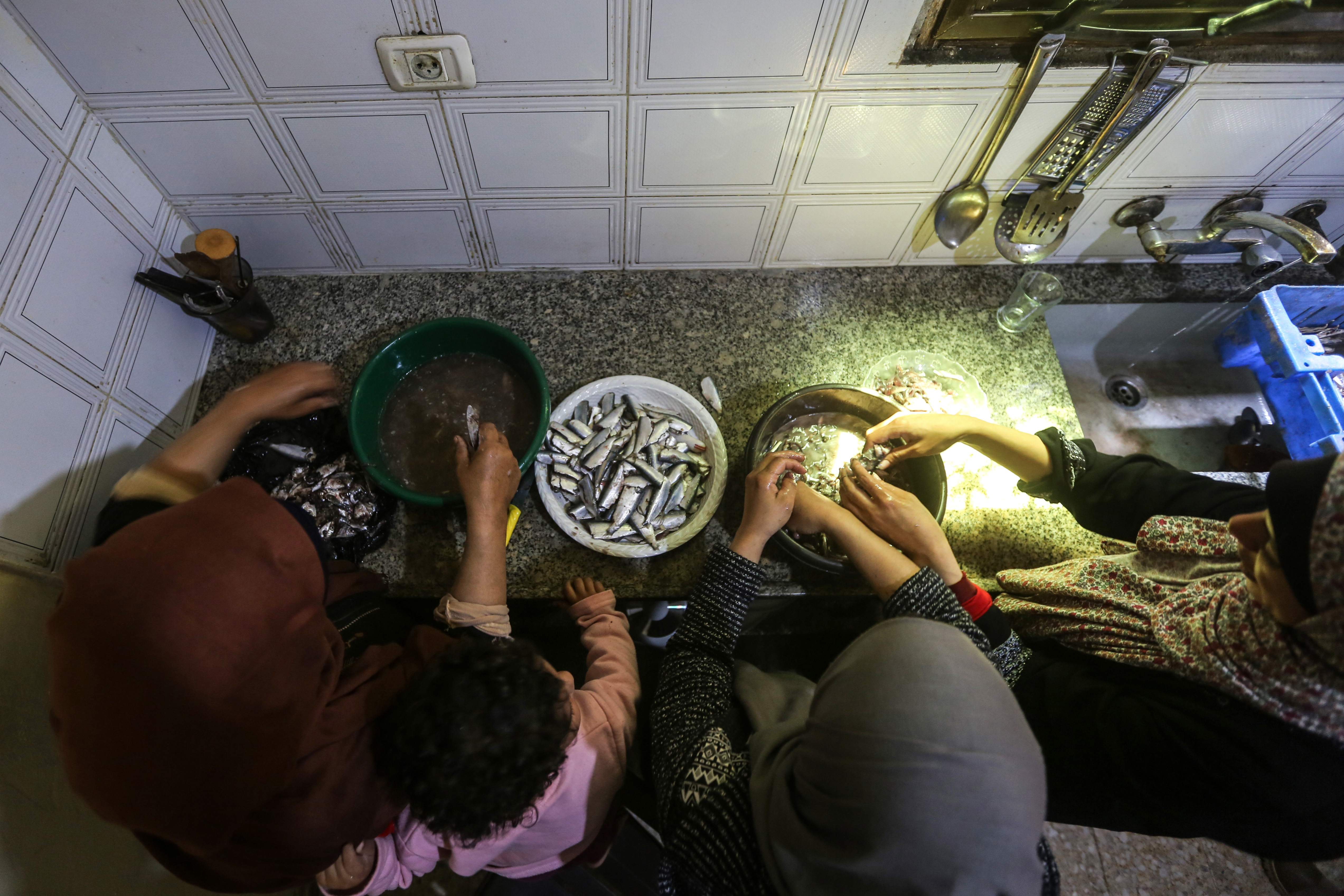 a view from above of Khadr's mother, his daughter Sandy, his sister, and Madelyn as they debone sardines