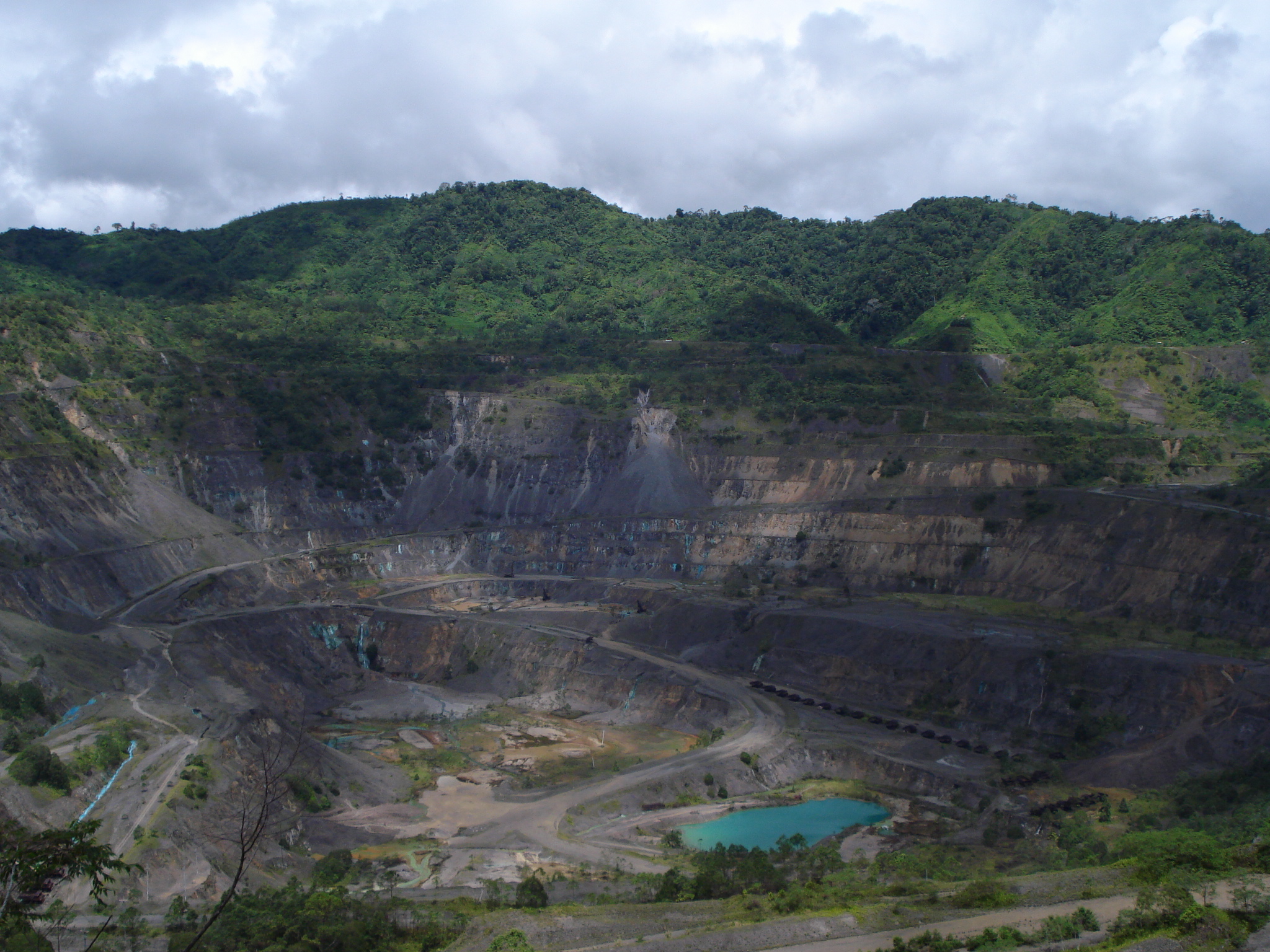 An aerial view of the abandoned Panguna mine surrounded by forest with a turquoise lake