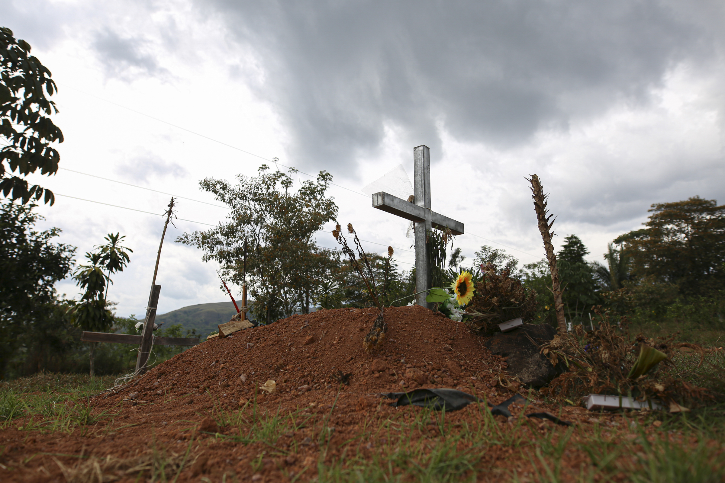 A photo of the grave of Sergio Rojas, with a cross on a little hill and a flower near the cross.
