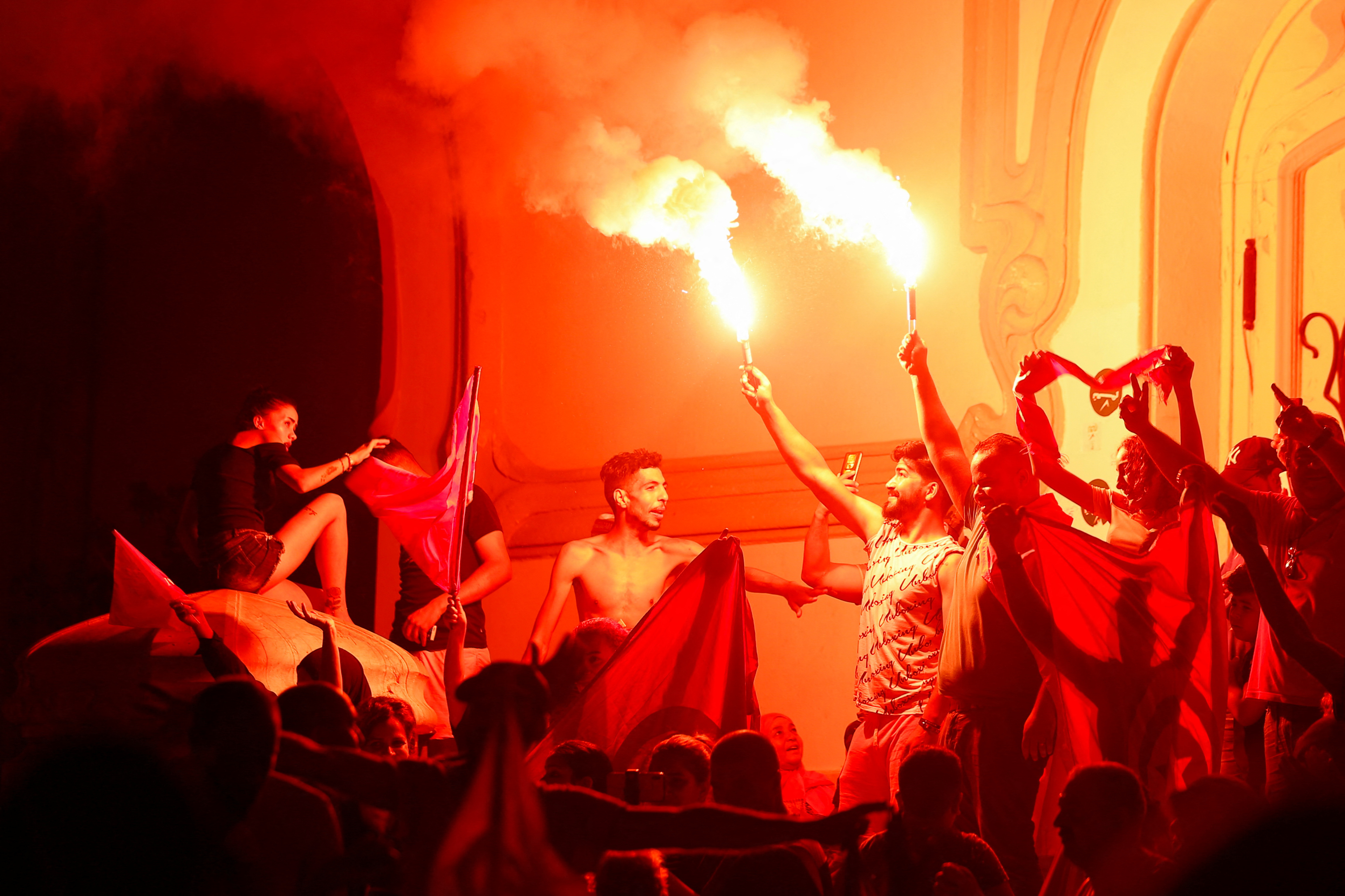 Supporters of president Kais Saied light flares as they celebrate after exit poll indicates voters backed his new constitution