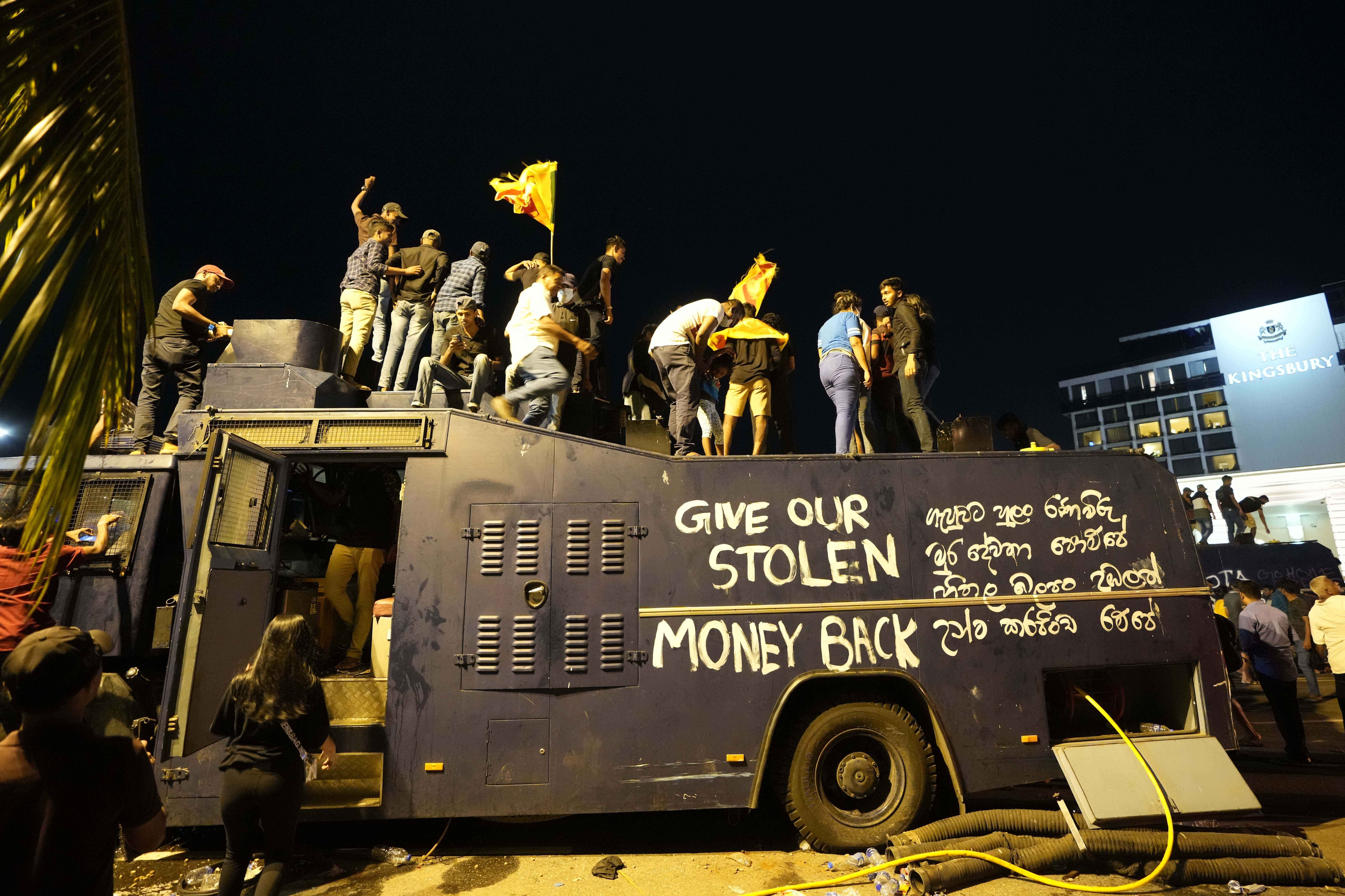 Protesters stand on a vandalised police water canon truck