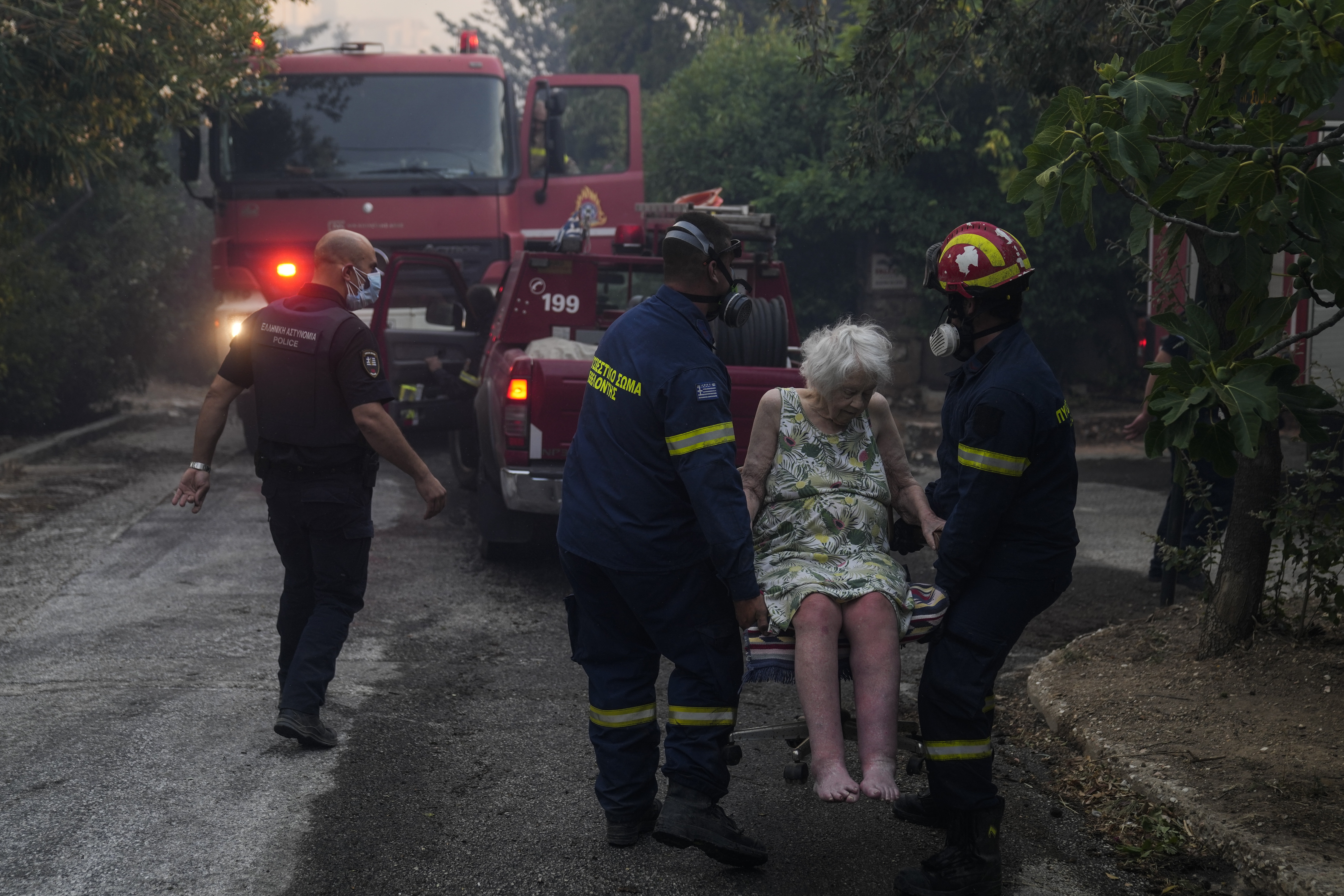 Firefighters evacuate an elderly woman from her house in Penteli,