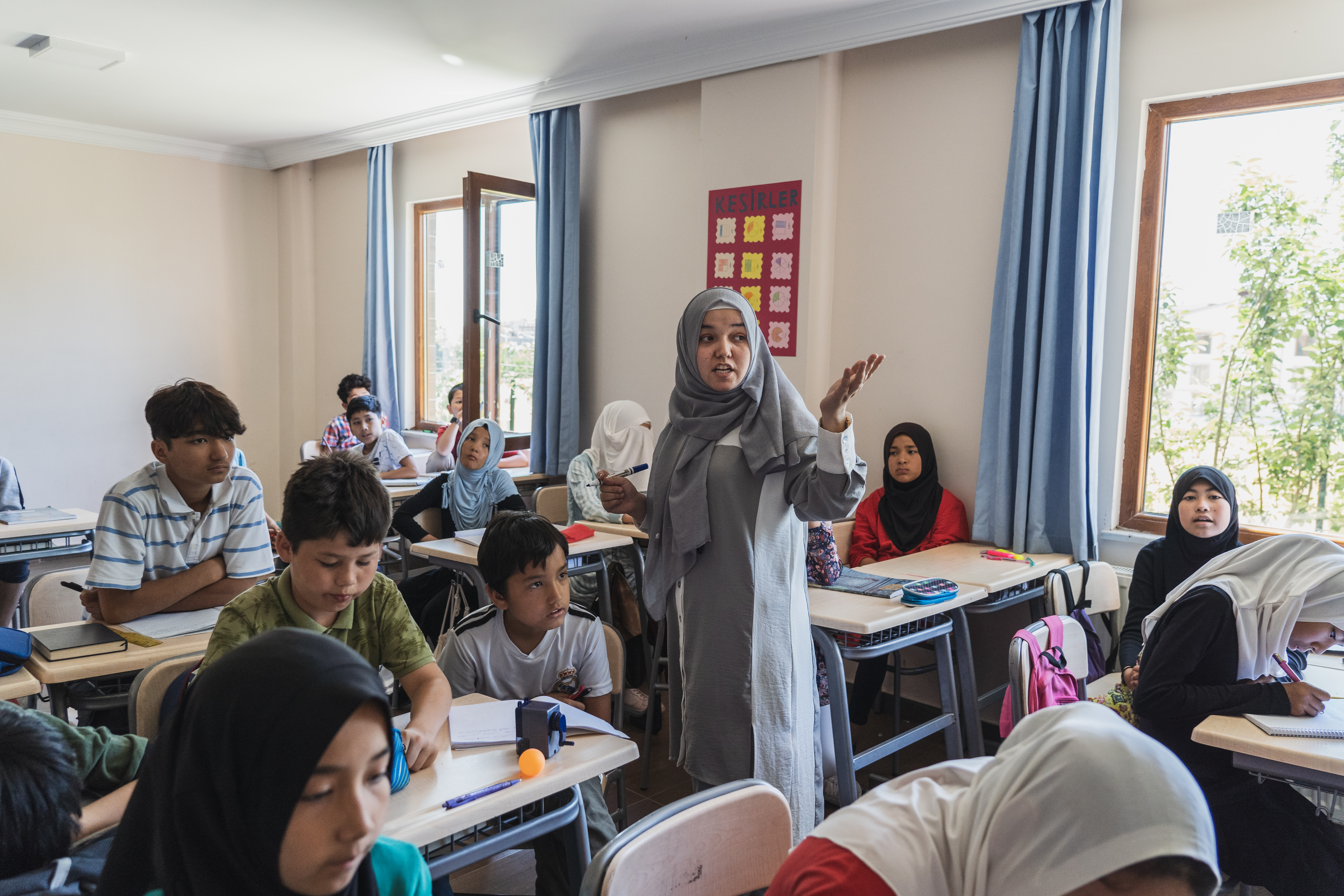 A photo of Omerjan standing between the students' desks and looking towards the front of the classroom.