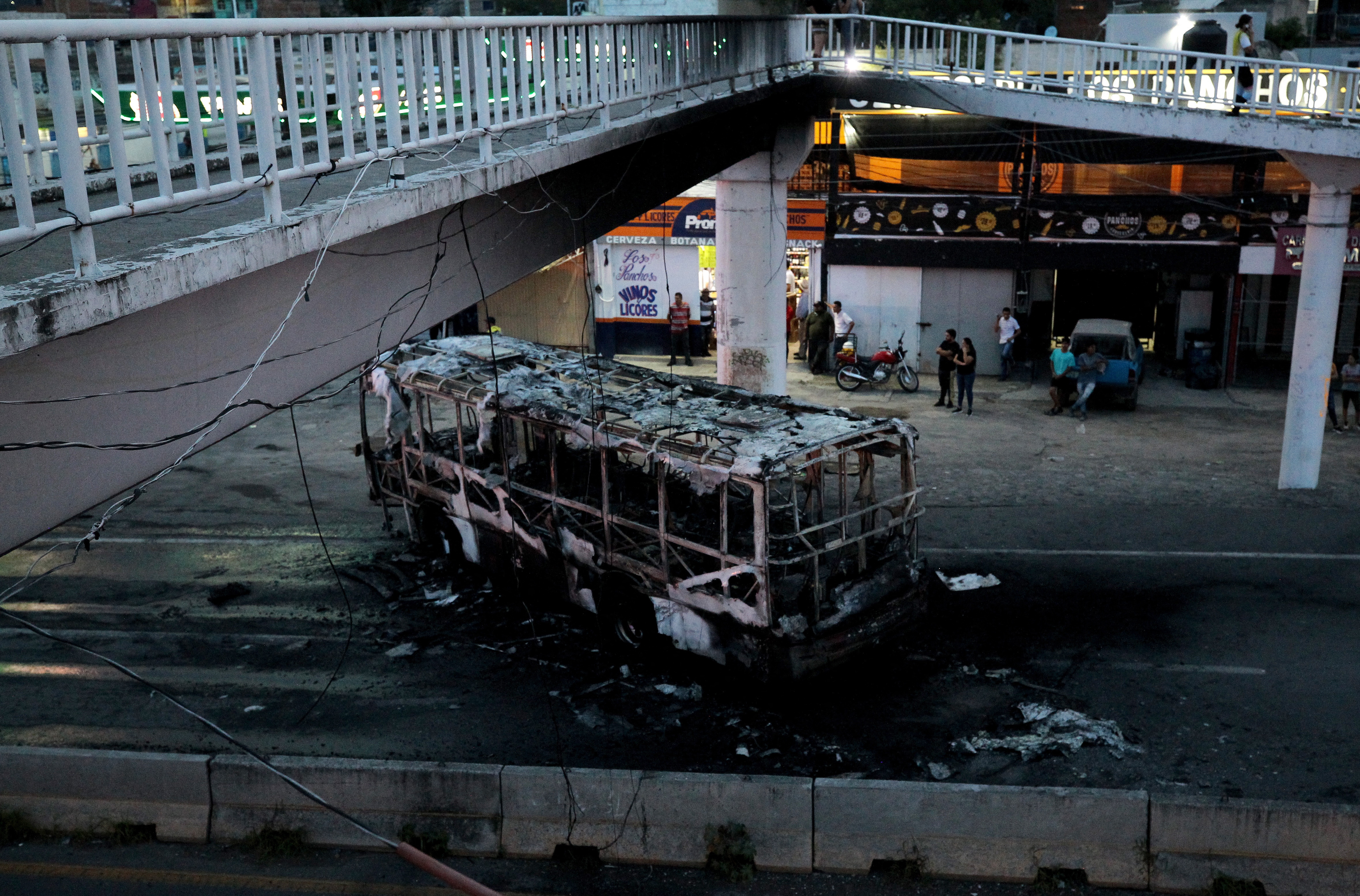 Members of the State Prosecutor's Office and Municipal Police guard the area where gang members set a bus on fire blocking a highway to prevent authorities from chasing them while they were clashing with another gang, in Zapopan, Jalisco State, Mexico, on August 9, 2022. - According to the authorities, no one was injured. (Photo by ULISES RUIZ / AFP)