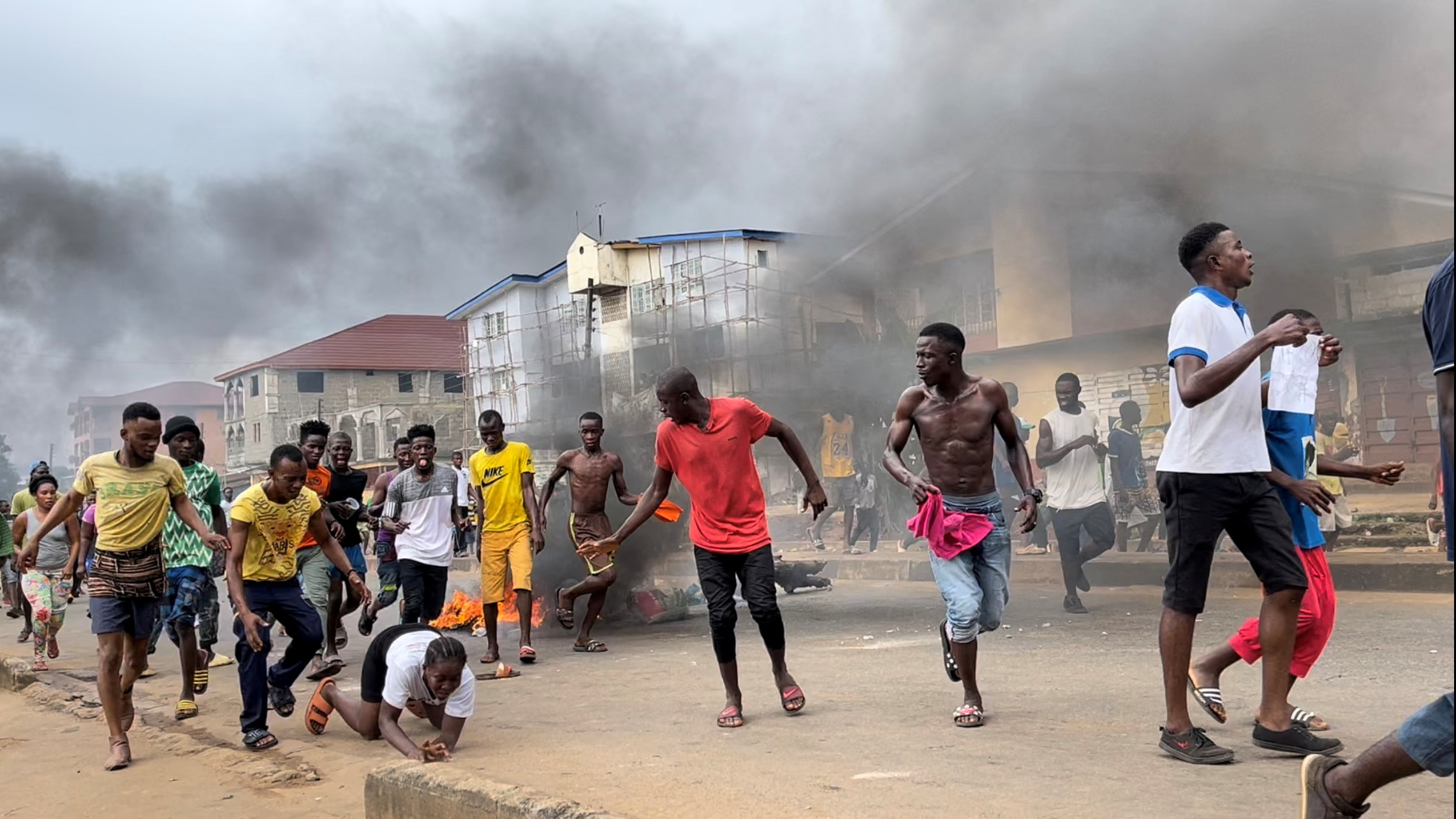 Sierra Leone protesters run among billowing smoke.