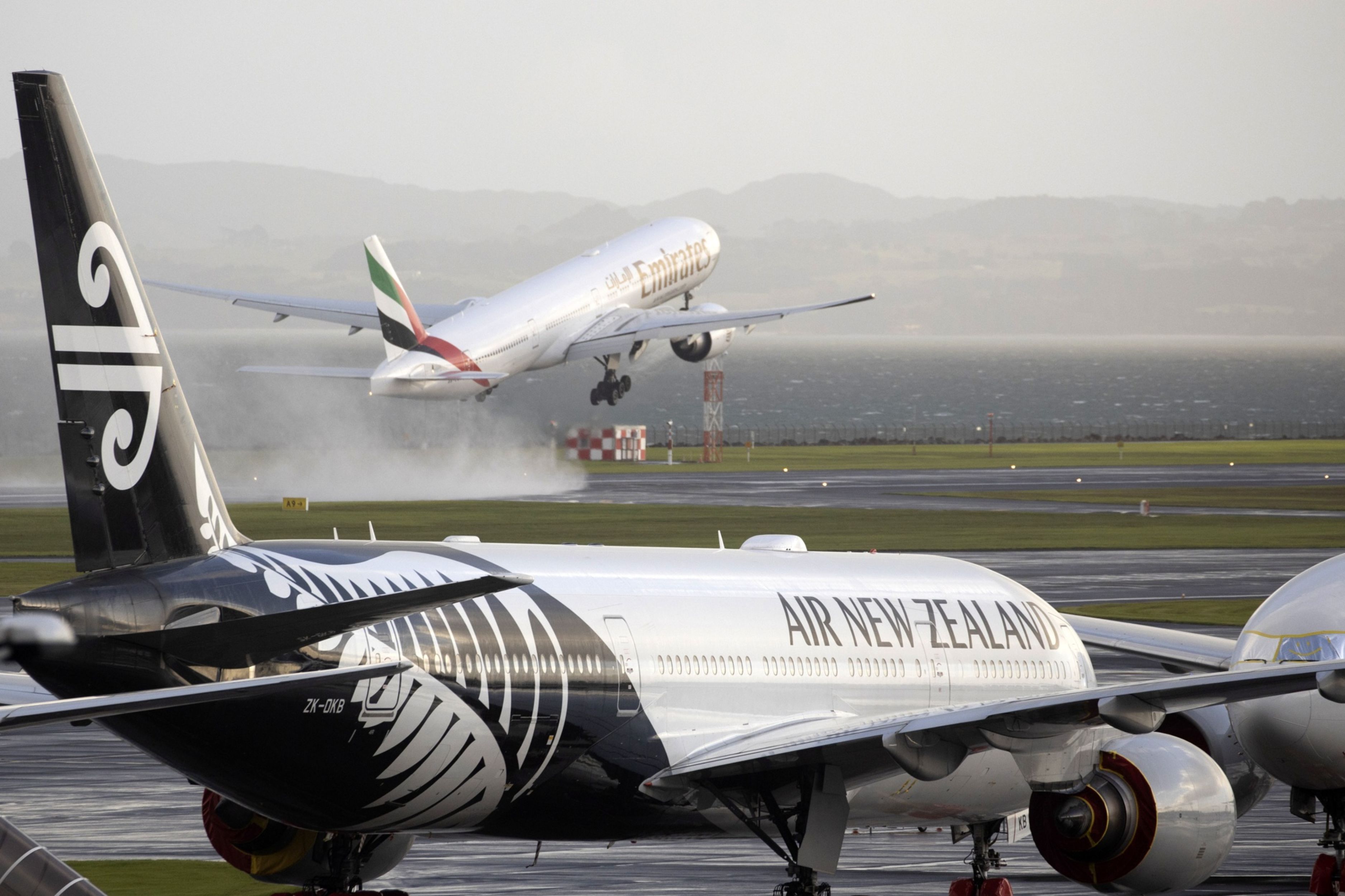 Air New Zealand plane on the tarmac in the foreground as another plane takes off from Auckland Airport in Auckland, New Zealand.