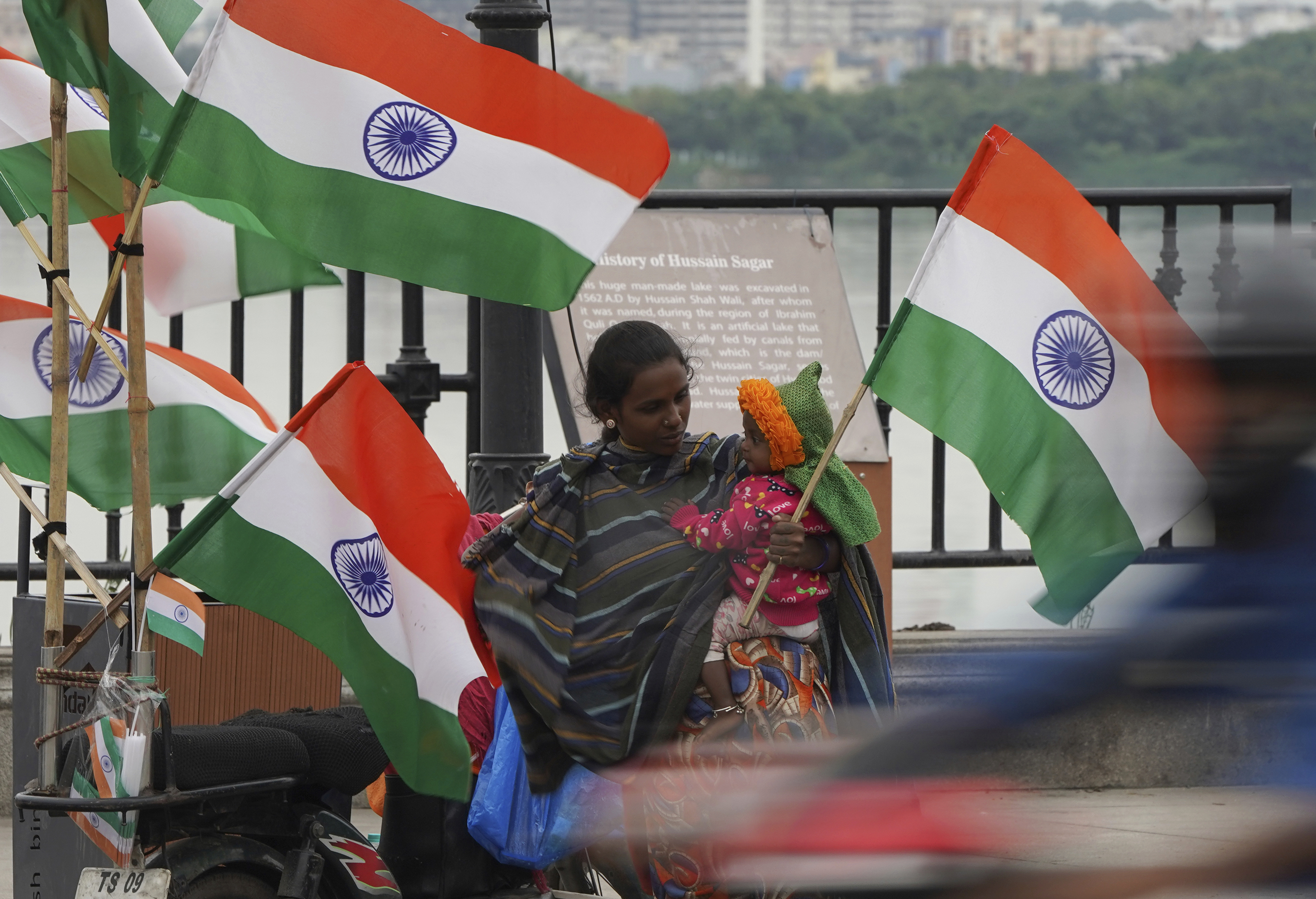 A roadside vendor carrying a child sells Indian flags