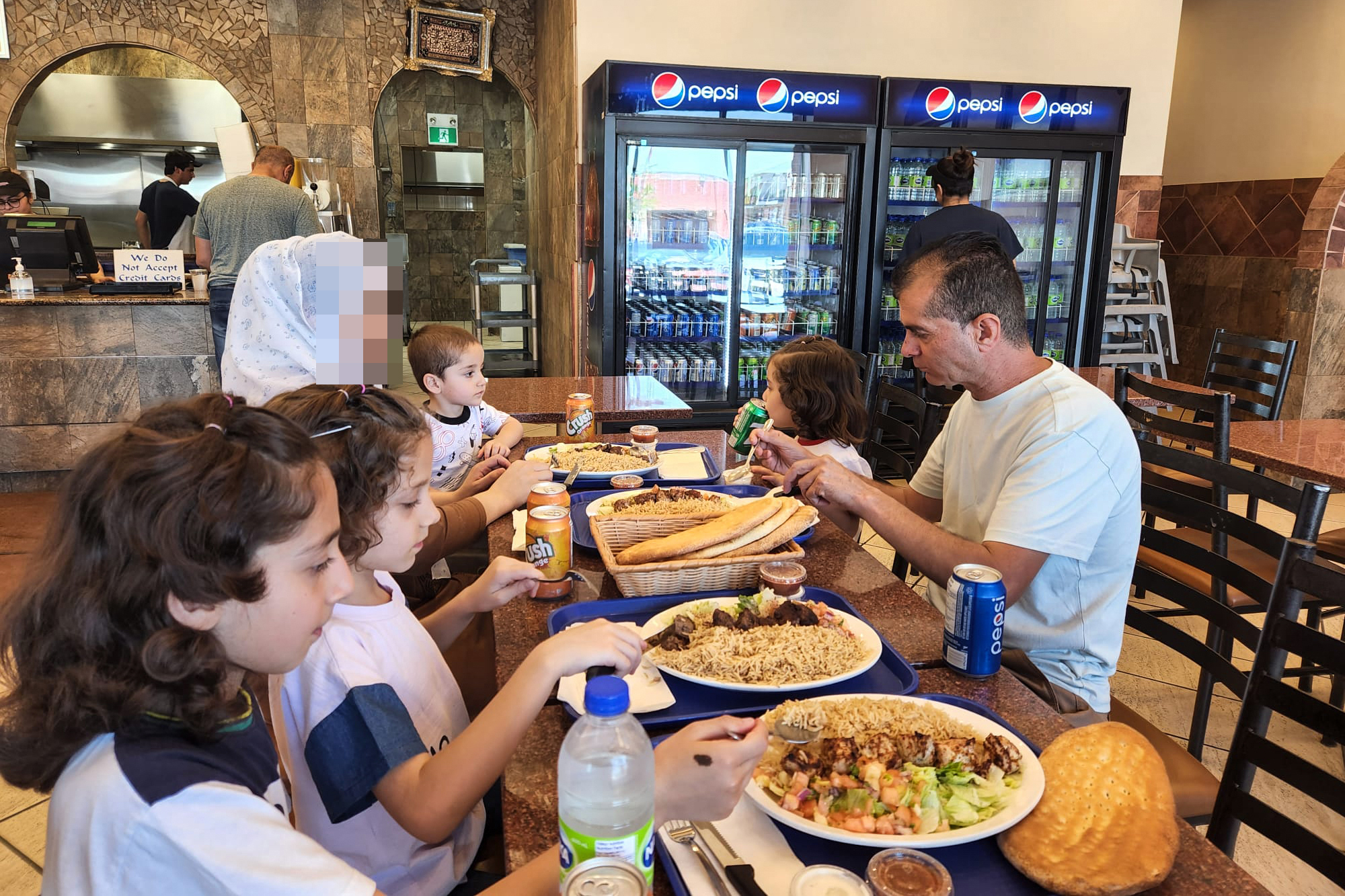 A man, woman, and four children sit at a table eating kebab and naan