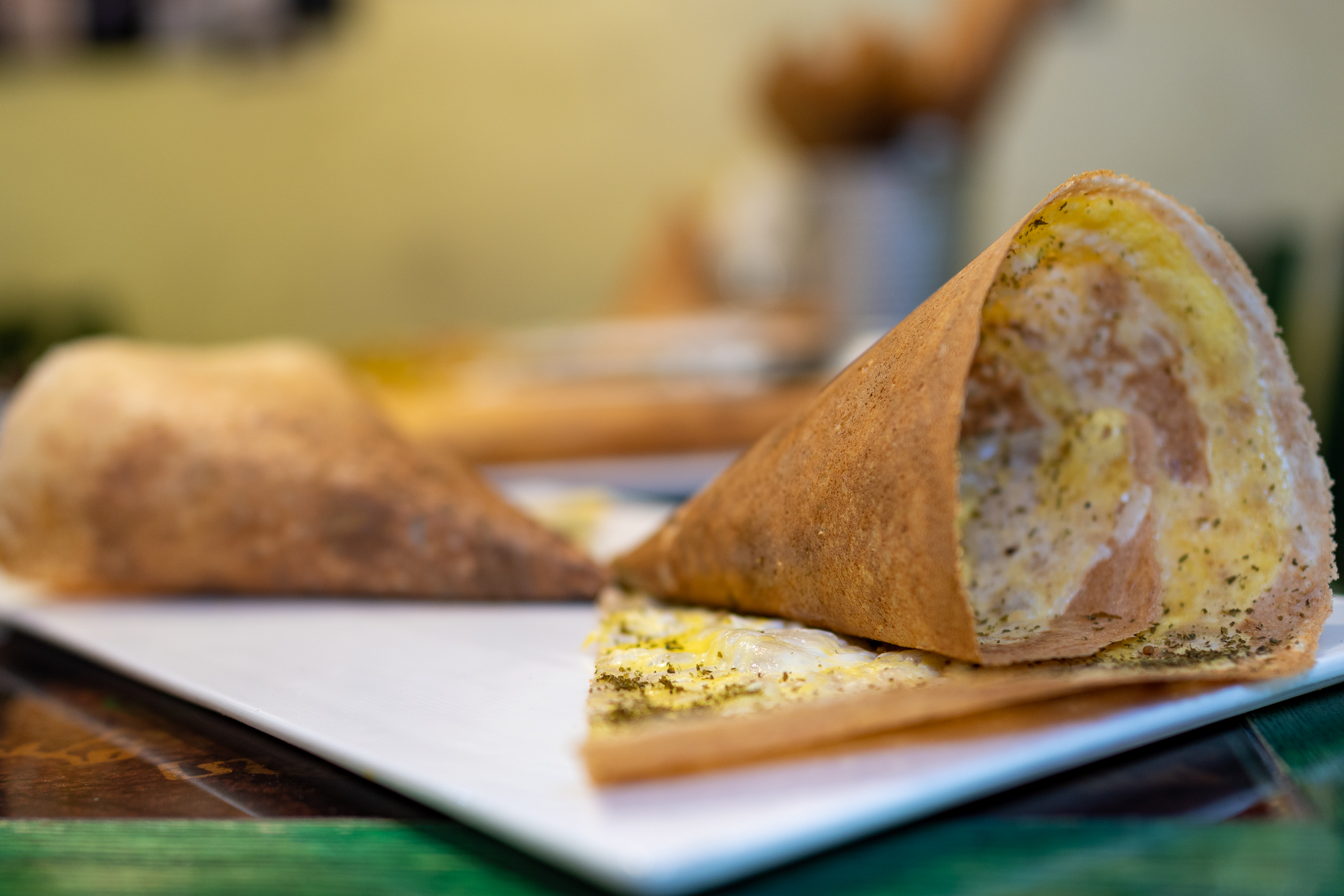 In focus is one half of a double cone of crisp regag bread. We can see the thin egg filling and a sprinkle of green zaatar