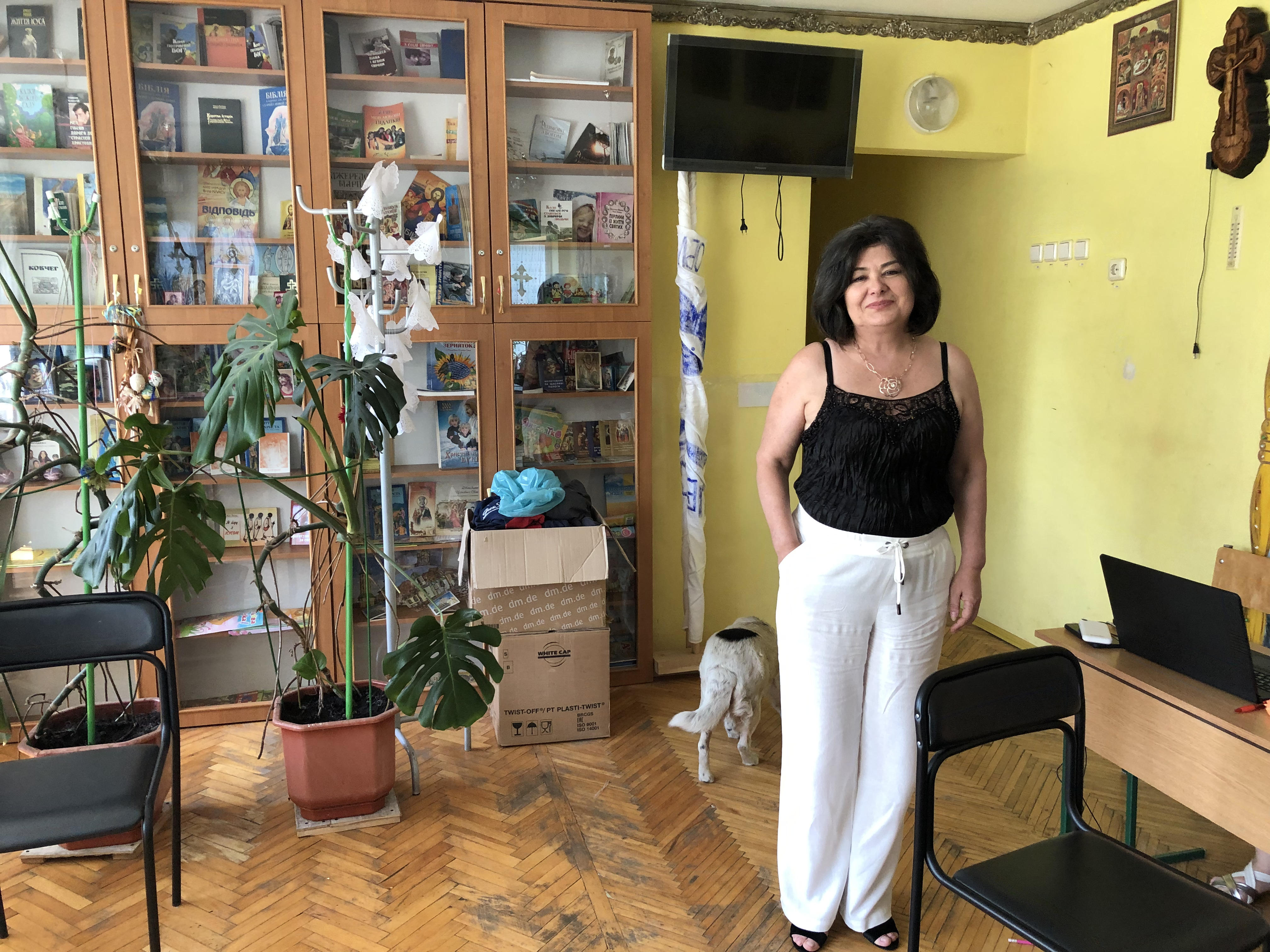 A photo of Svitlana Havrilyuk standing on one side of a room with a desk next to her and a shelf behind her.