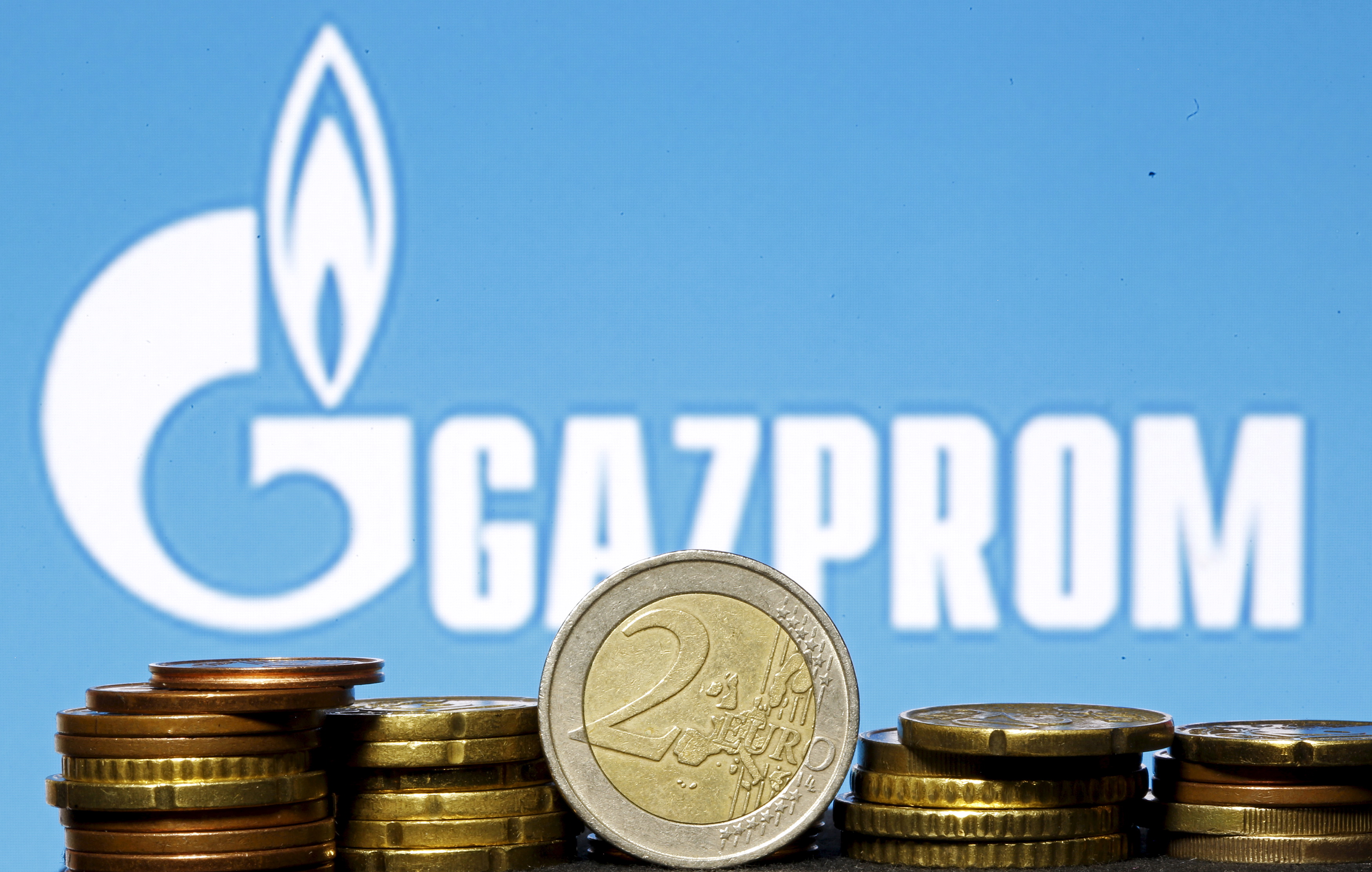 Euro coins are seen in front of displayed logo of Gazprom