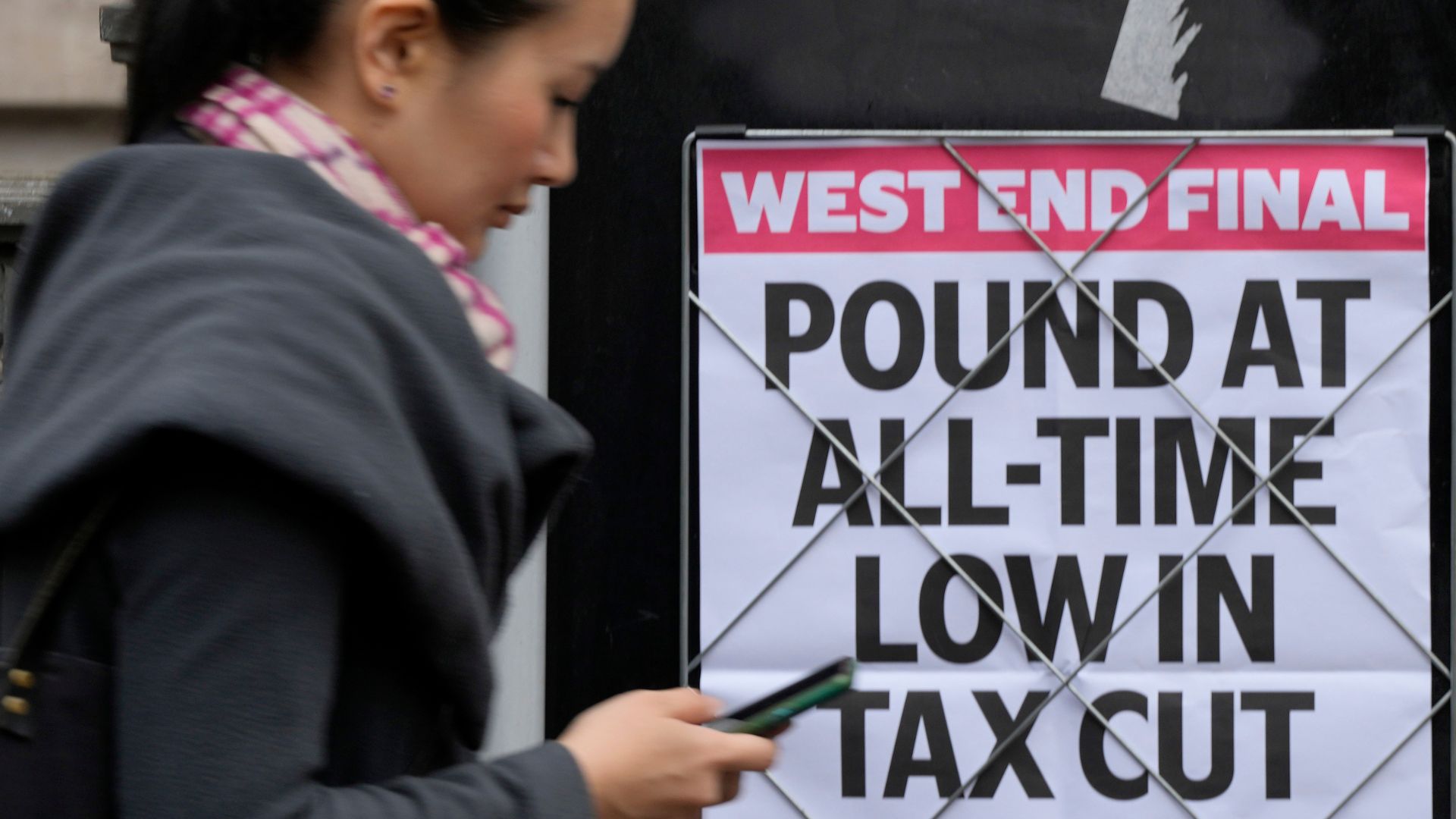 A woman walks past a headline posted on a wall announcing the Pound at an all time low