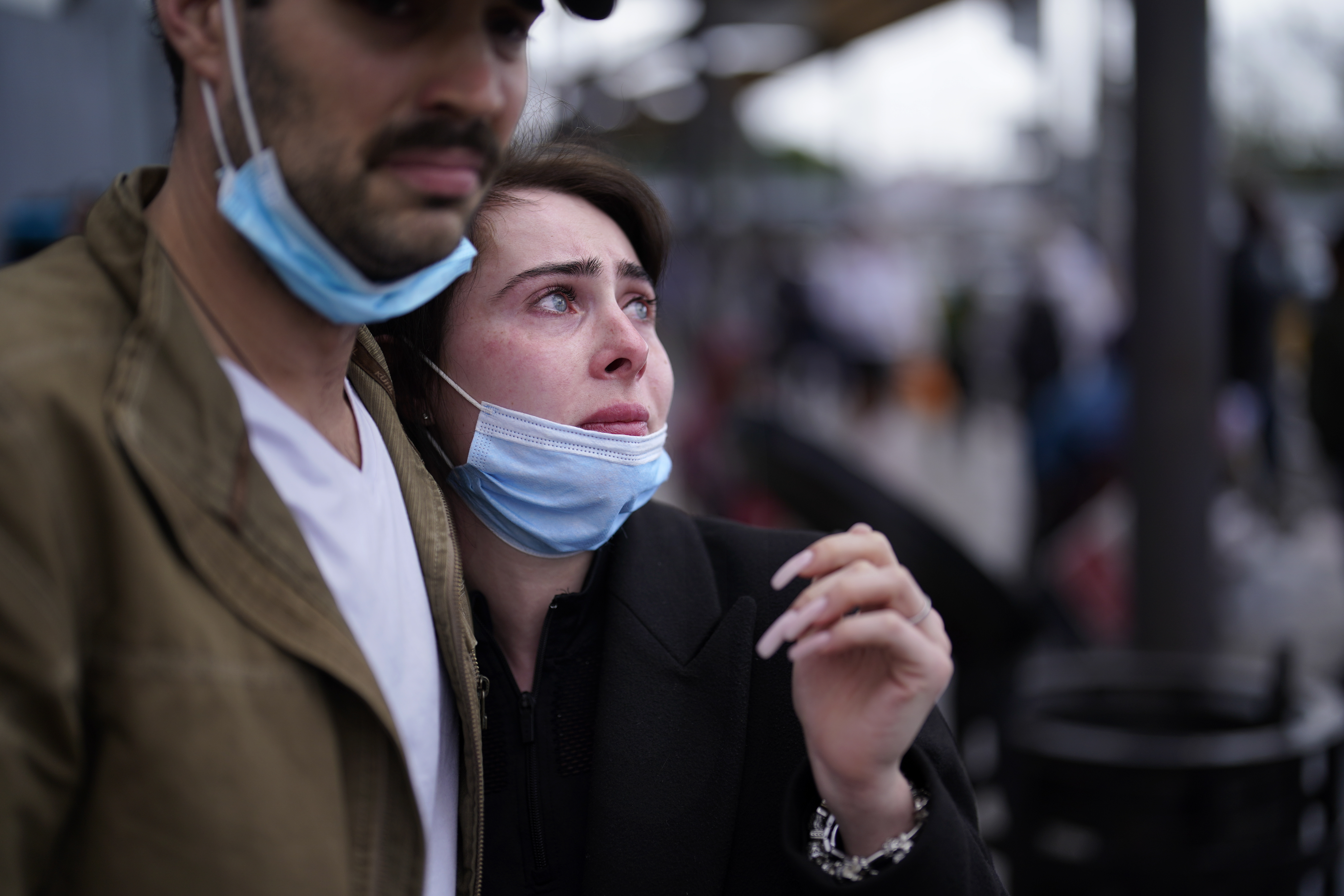Close up of husband with his arm around wife who is leaning into him – both are wearing masks
