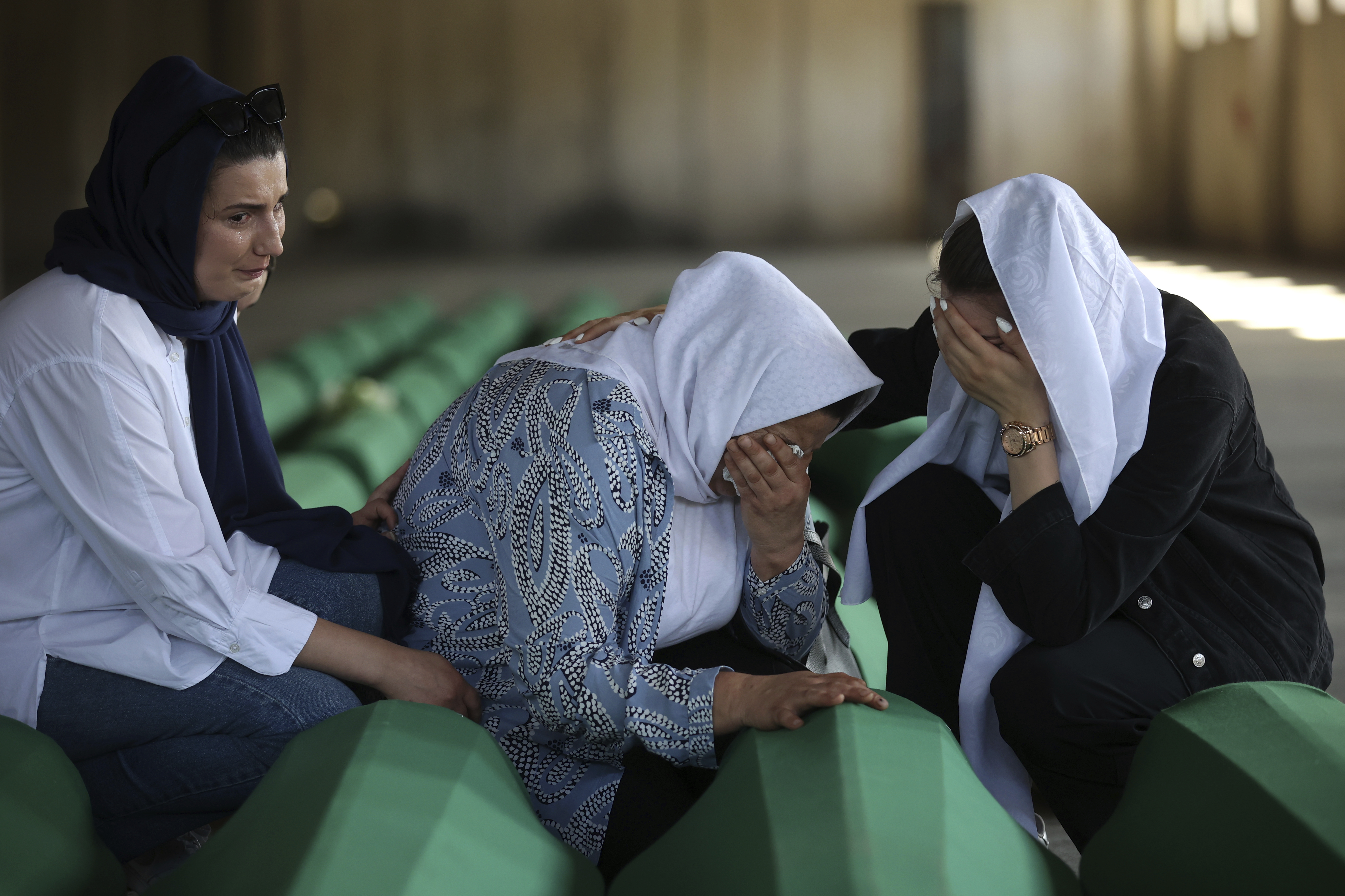 Bosnian muslim women mourn next to the coffin containing remains of their family member who is among 50 newly identified victims of Srebrenica Genocide in Potocari, Bosnia, Sunday, July 10, 2022. Thousands converge on the eastern Bosnian town of Srebrenica to commemorate the 27th anniversary on Monday of Europe's only acknowledged genocide since World War II. (AP Photo/Armin Durgut)
