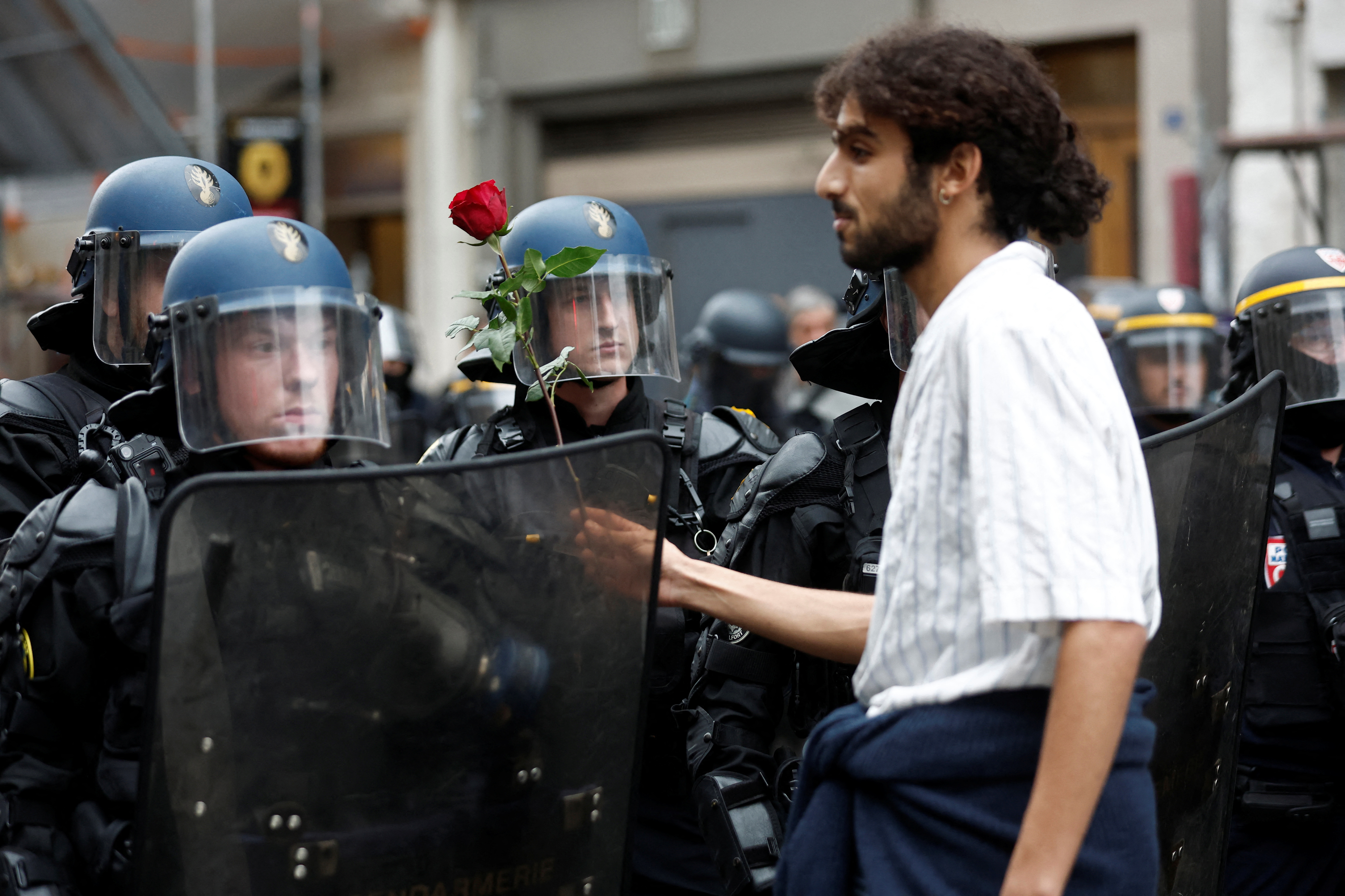 Protester offering a red rose to police who have their shields up