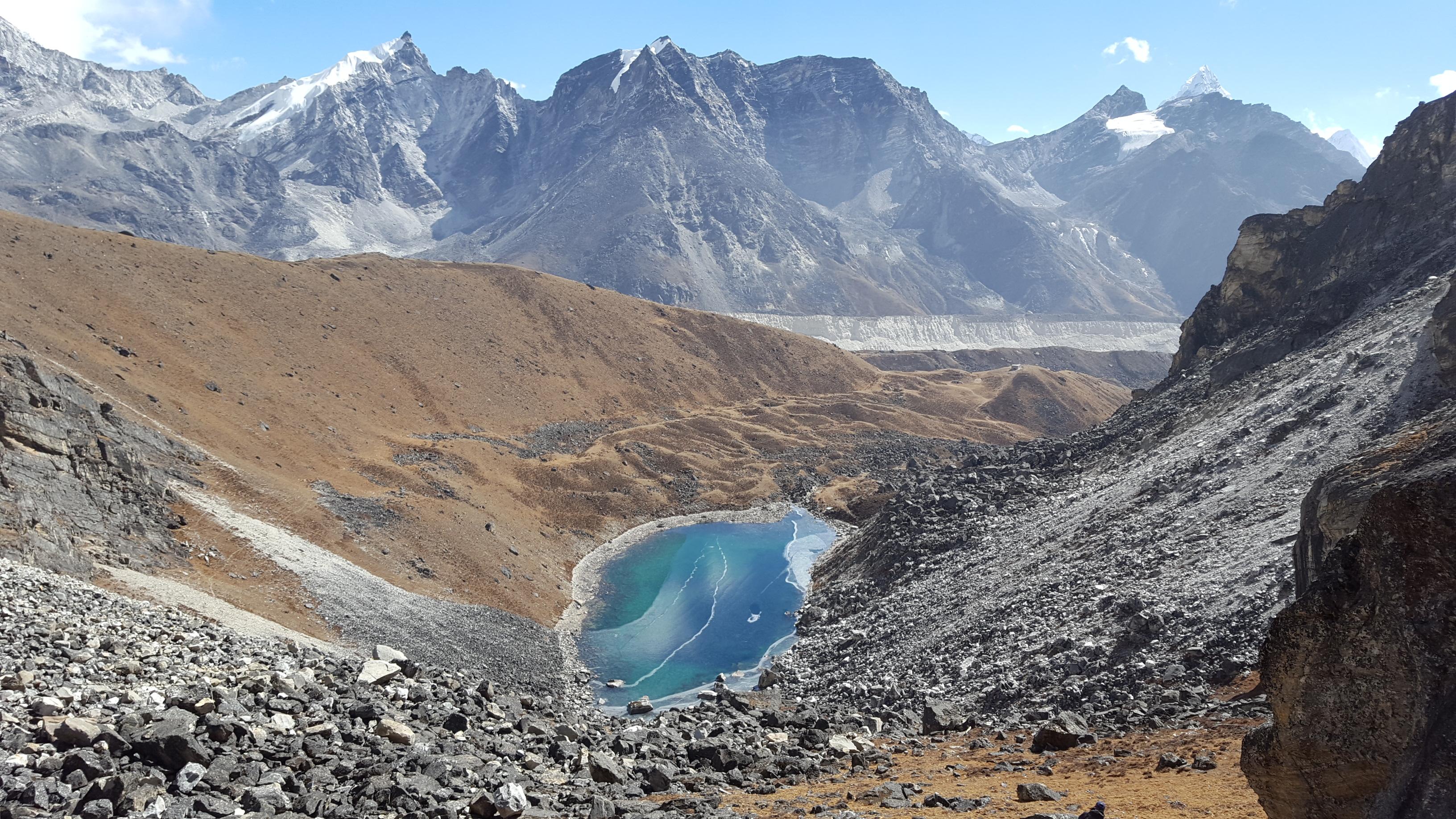 A photo of the Lobuche moraines with a small body of water and with mountains in the background.