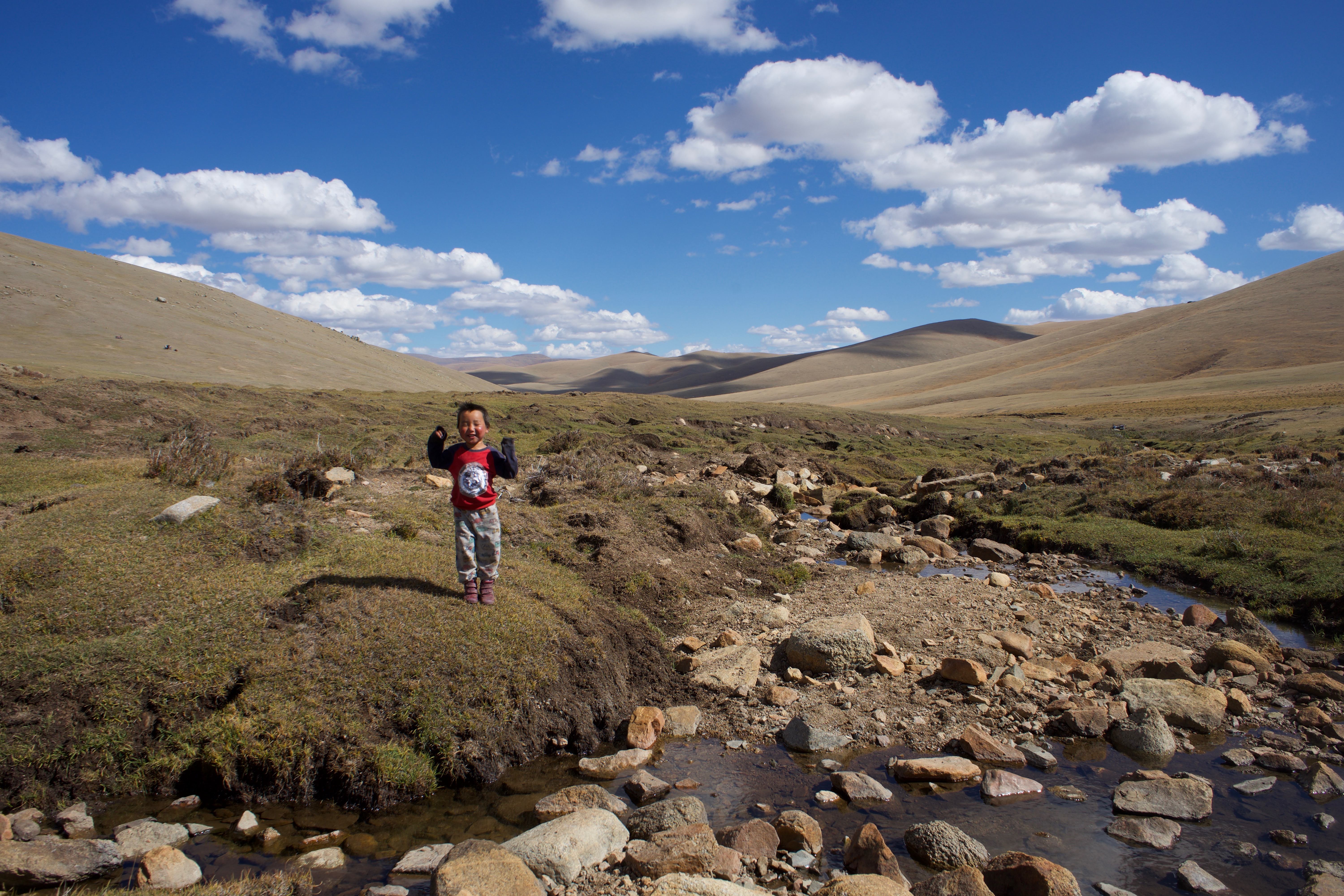 Myagmar-Ochir, 3, playing on the steppe next to a stream. He looks happy and excited.