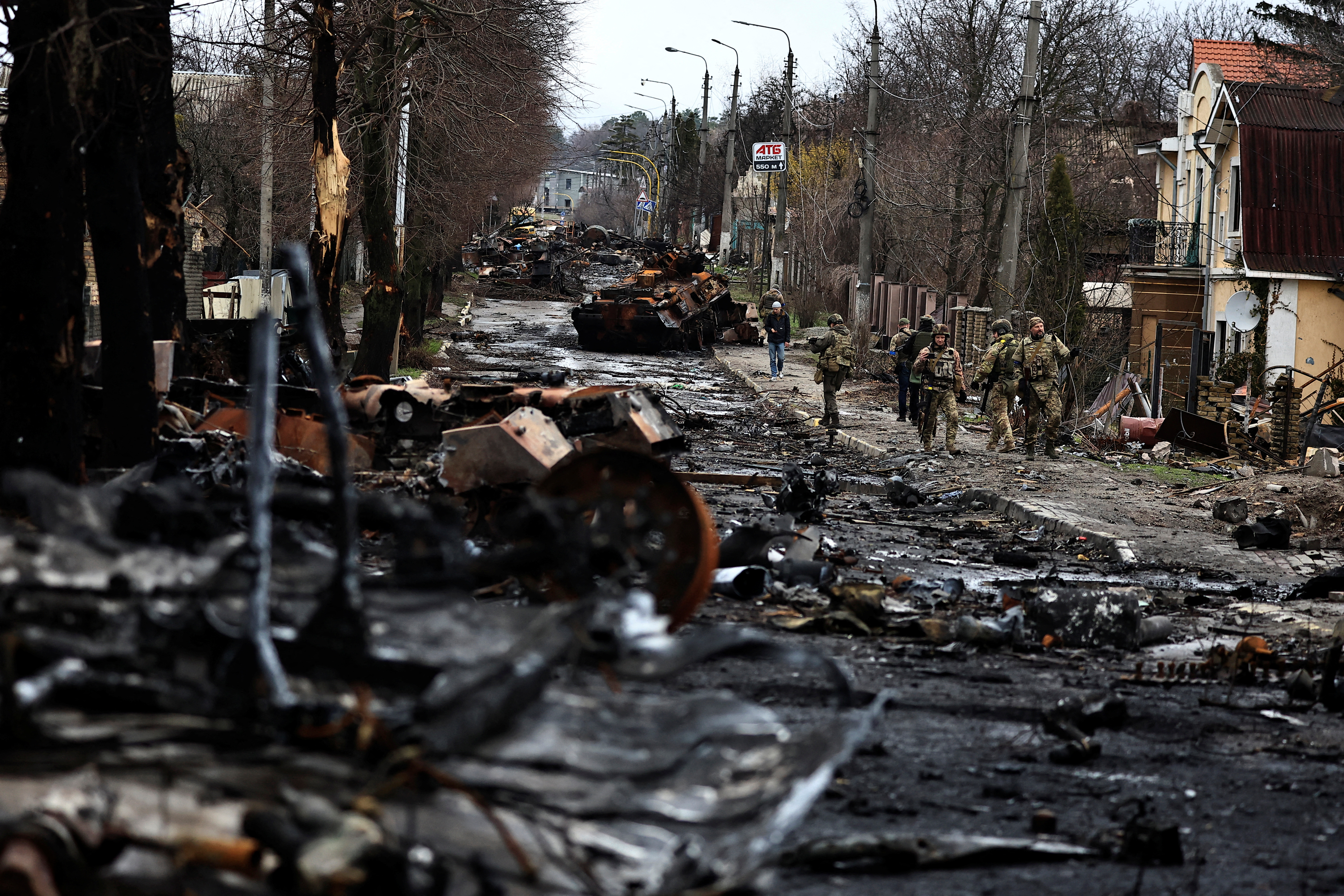 Soldiers walk past a destroyed Russian tank