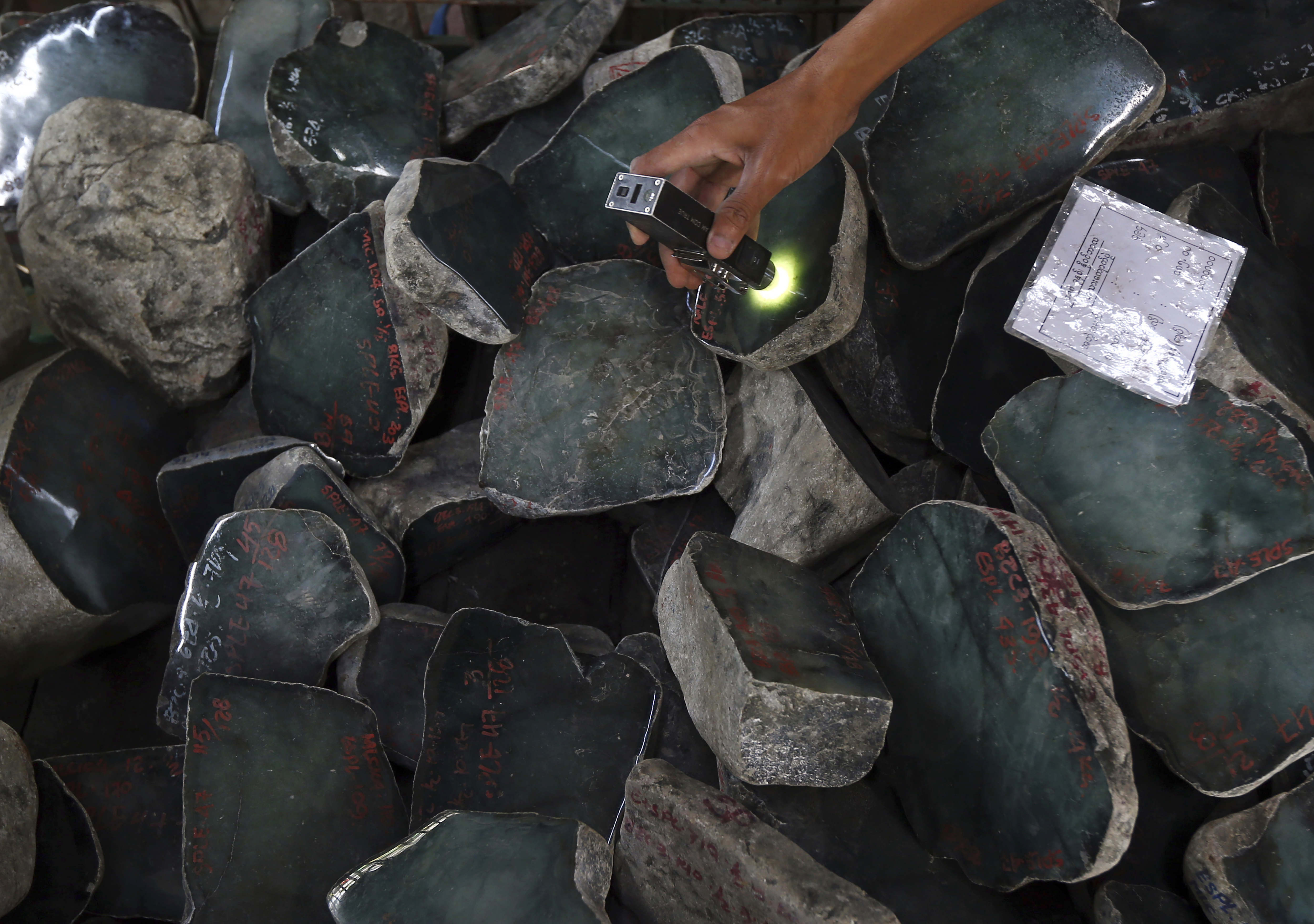 A close-up of piles of uncut jade stones at a gems emporium in Myanmar. A merchant is examining the rocks with a light