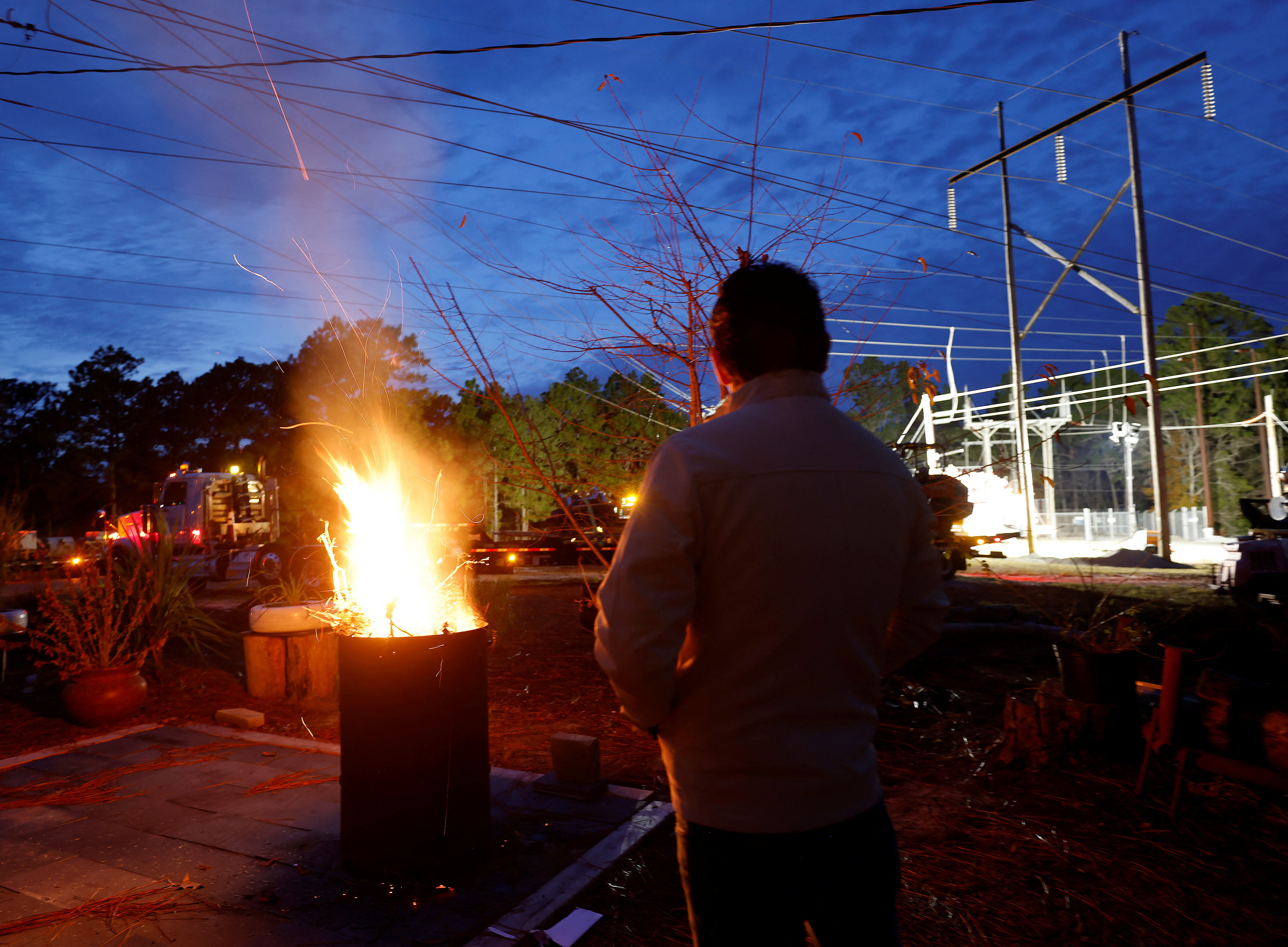 A man stands next to a fire as he watches repair work